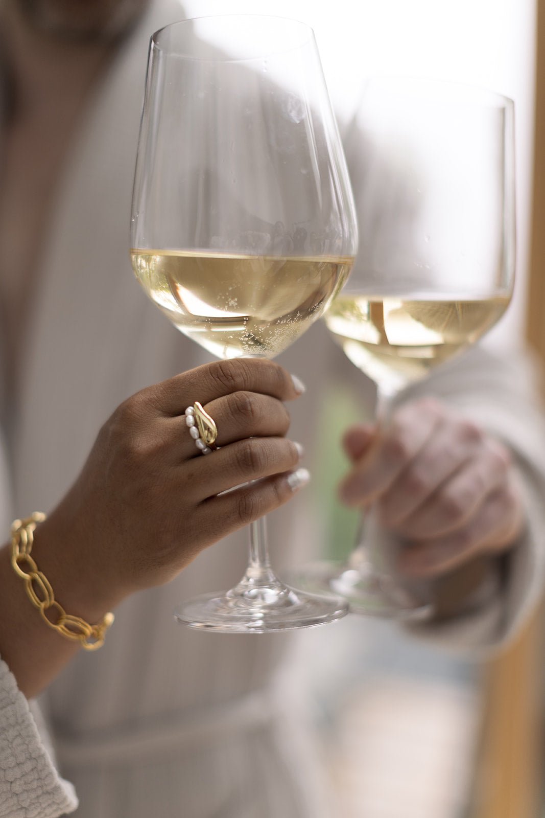 A couple toasts with white wine. The woman wearing freshwater pearl ring, gold-filled ring, and gold-filled girlfriend bracelet.