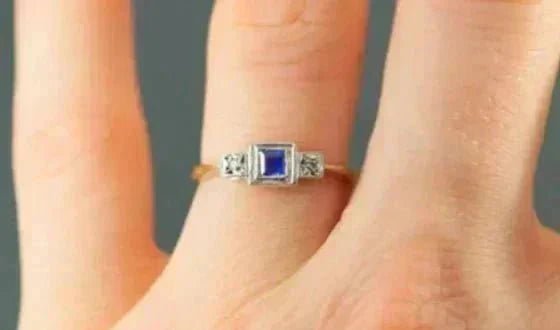 Close up of a gold vintage engagement ring with central sapphire on a ring finger with blurred background