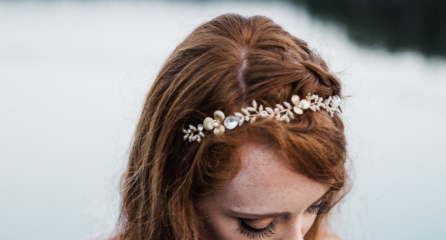 A bride looks down showing off her bridal headband while standing in the water of a lake.