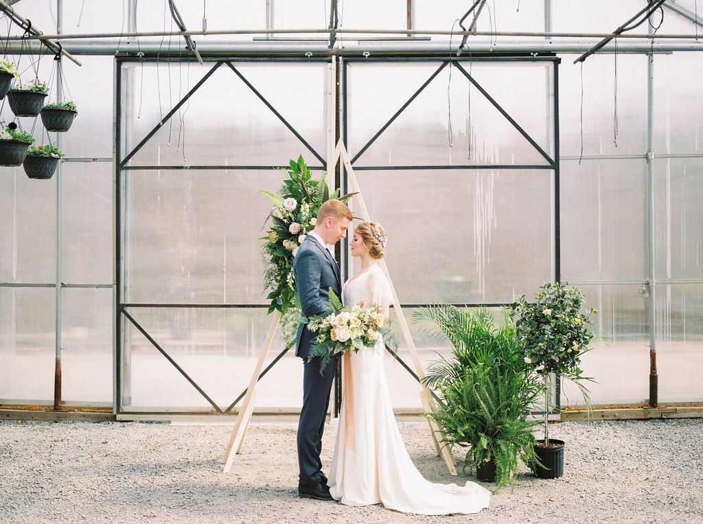 A bride and groom come together inside a large greenhouse.