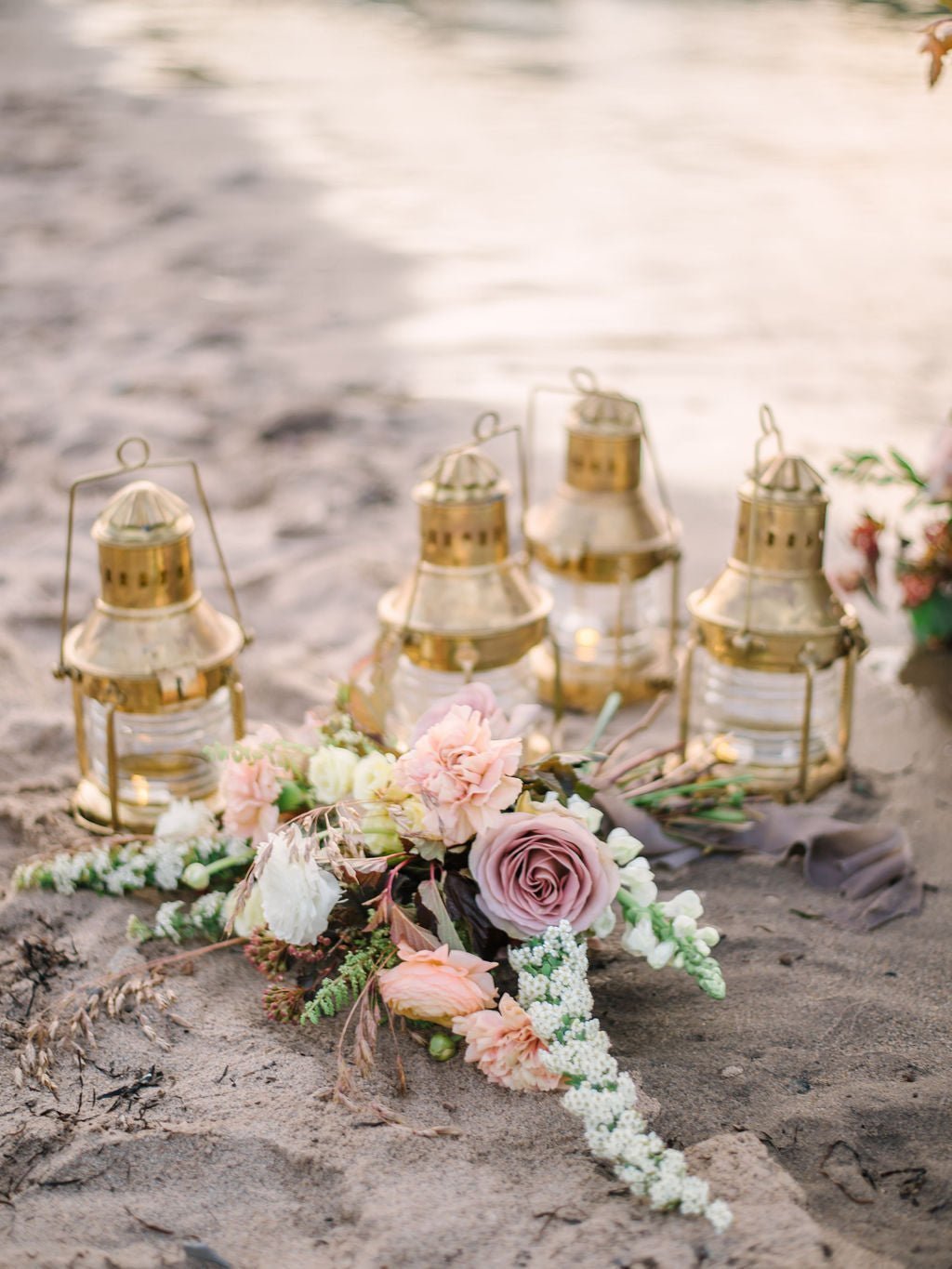 Four golden lanterns with a flower bouquet on beach sand.