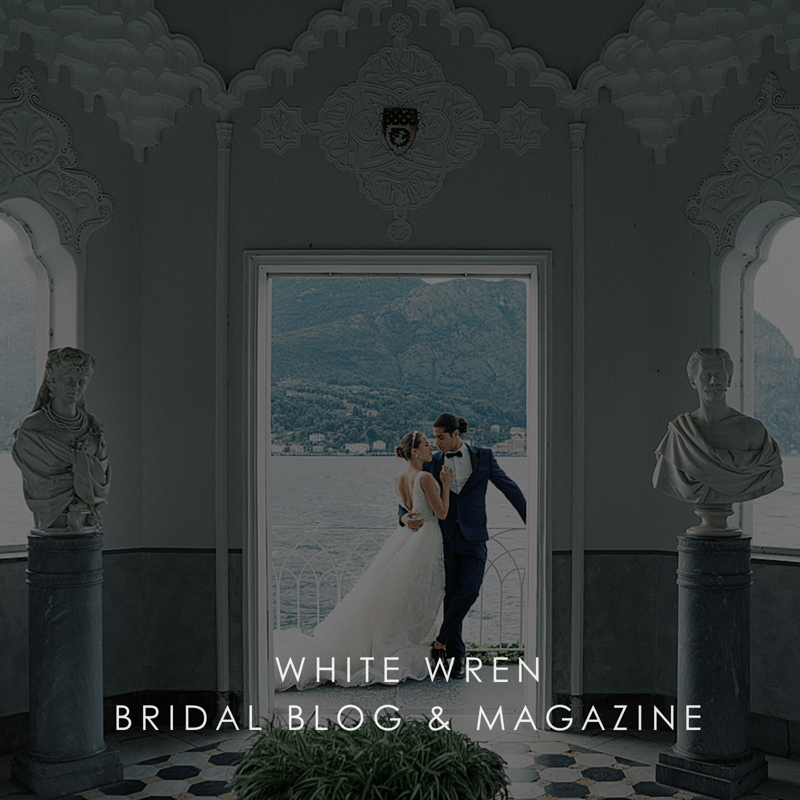 Couple in wedding attire standing in a decorative room with statues and a scenic view.