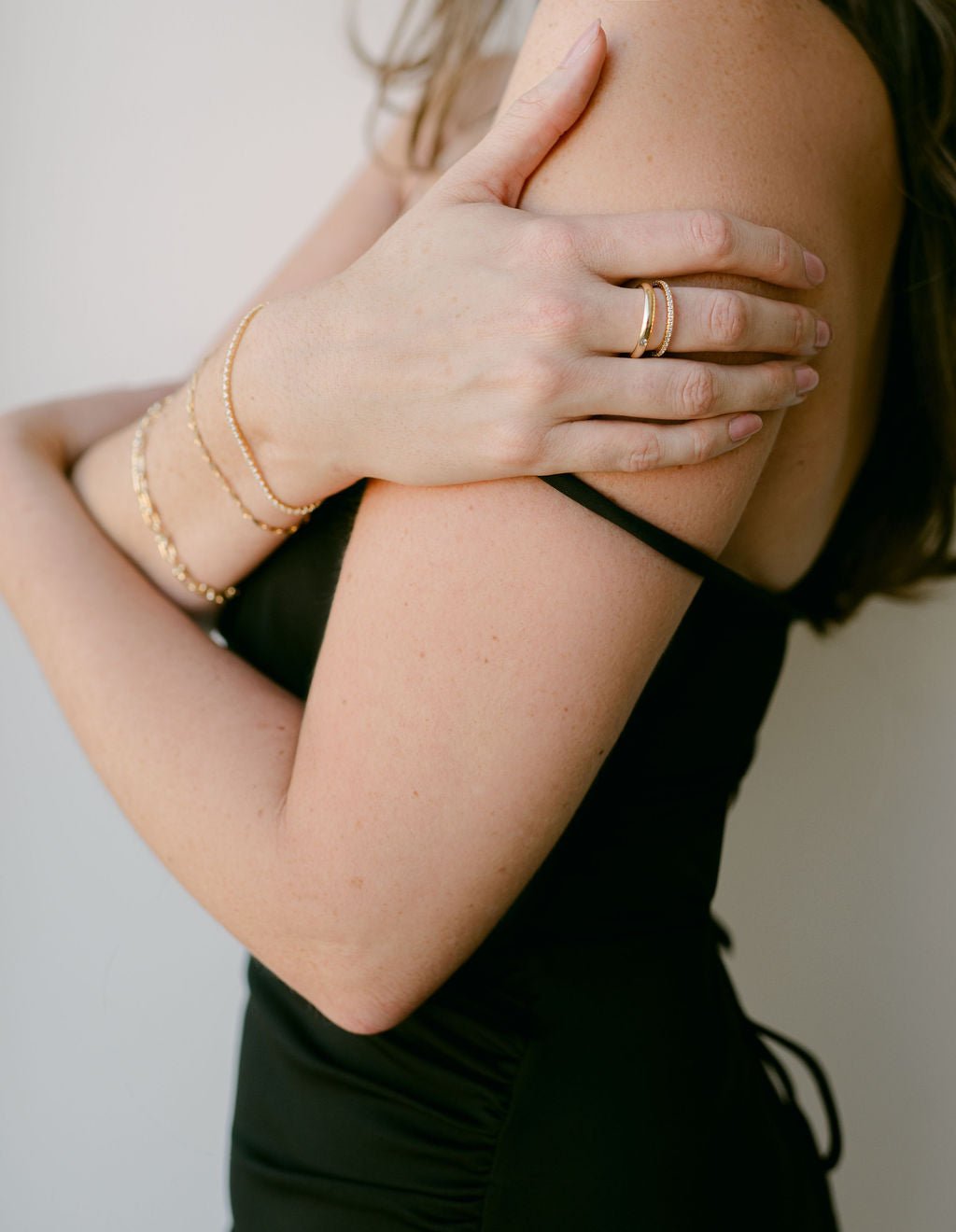Woman in slinky black dress wearing three gold filled bracelets and two gold rings on a neutral background. Gold-filled jewelry & handmade everyday jewelry by Canadian jewelry designer