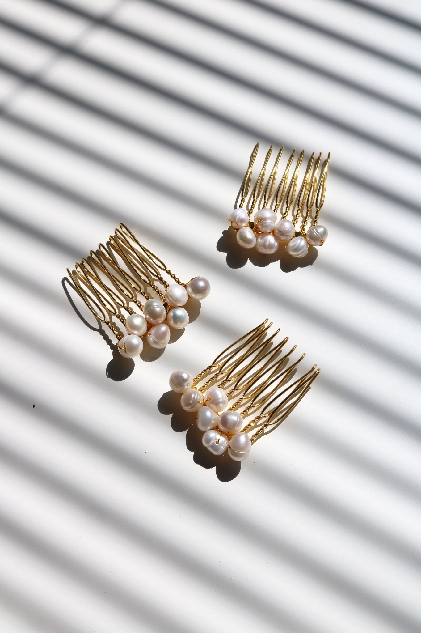 Three gold hair combs with freshwater pearls on a white surface with striped shadows. Perfect Pearl Bridal jewelry, Canada handmade. Bridal Hair Accessories with freshwater pearls.