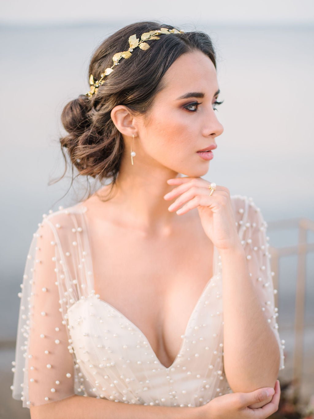 Thoughtful bride contemplates while displaying a beautiful golden hair circlet with dainty freshwater pearls and crystals among glistening leaves. Bridal Hair Accessories. Bridal Accessories. Canadian Bridal Accessories. Handmade Canadian Accessories. Canadian handmade Accessories. Canadian weddings. Wedding Canada. Organic pearl accessories. Pearl Bridal Hair Accessories. Pearl Bridal Accessories.