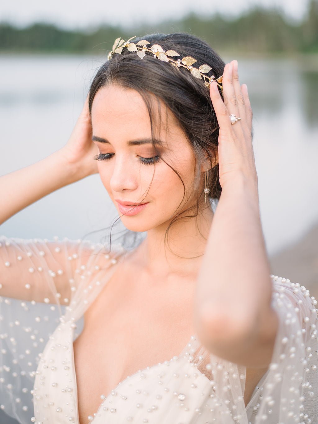 Bride in a white tulle and pearl wedding dress adjusting golden leaf bridal hair circlet with freshwater pearls and crystals with water background. Handmade bridal accessories, Canadian bridal accessories, & bridal hairpiece Canada