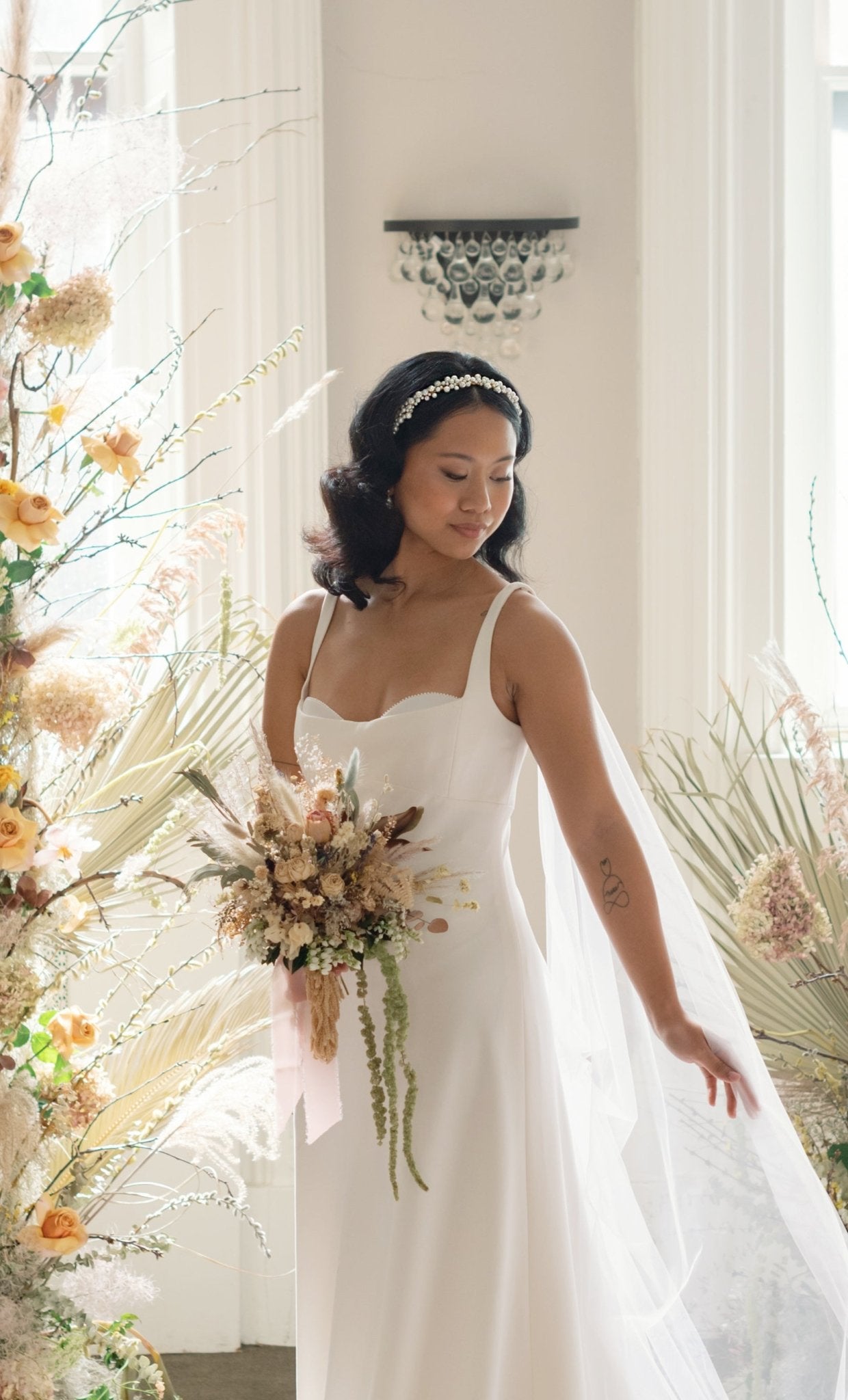 Flattering photo of a bride holding wedding bouquet while in a white wedding gown wears a headband of large clustered freshwater pearls. Organic pearl jewelry. Canadian bridal jewelry. Woman-owned Canadian jewelry brand. Bridal hair accessories. Bridal Accessories. Bridal jewelry Canada. Pearl jewelry Canada. Pearl Bridal jewelry Canada. Handmade Canadian jewelry.