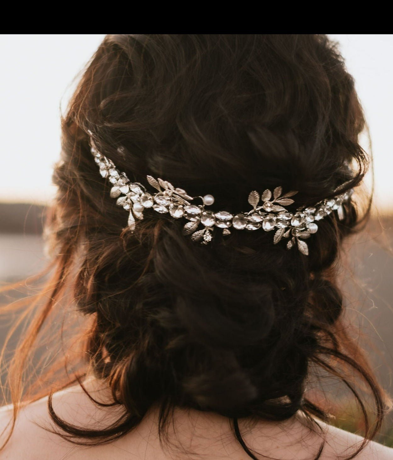 Silver Anwen Crystal & Leaf Crown Bridal Hair Accessory Sitting on Top of Curly Dark Hair Bun. Bridal Hair Accessories. Bridal Accessories. Canadian Bridal Accessories. Handmade Canadian Accessories. Canadian handmade Accessories. Canadian weddings. Wedding Canada.