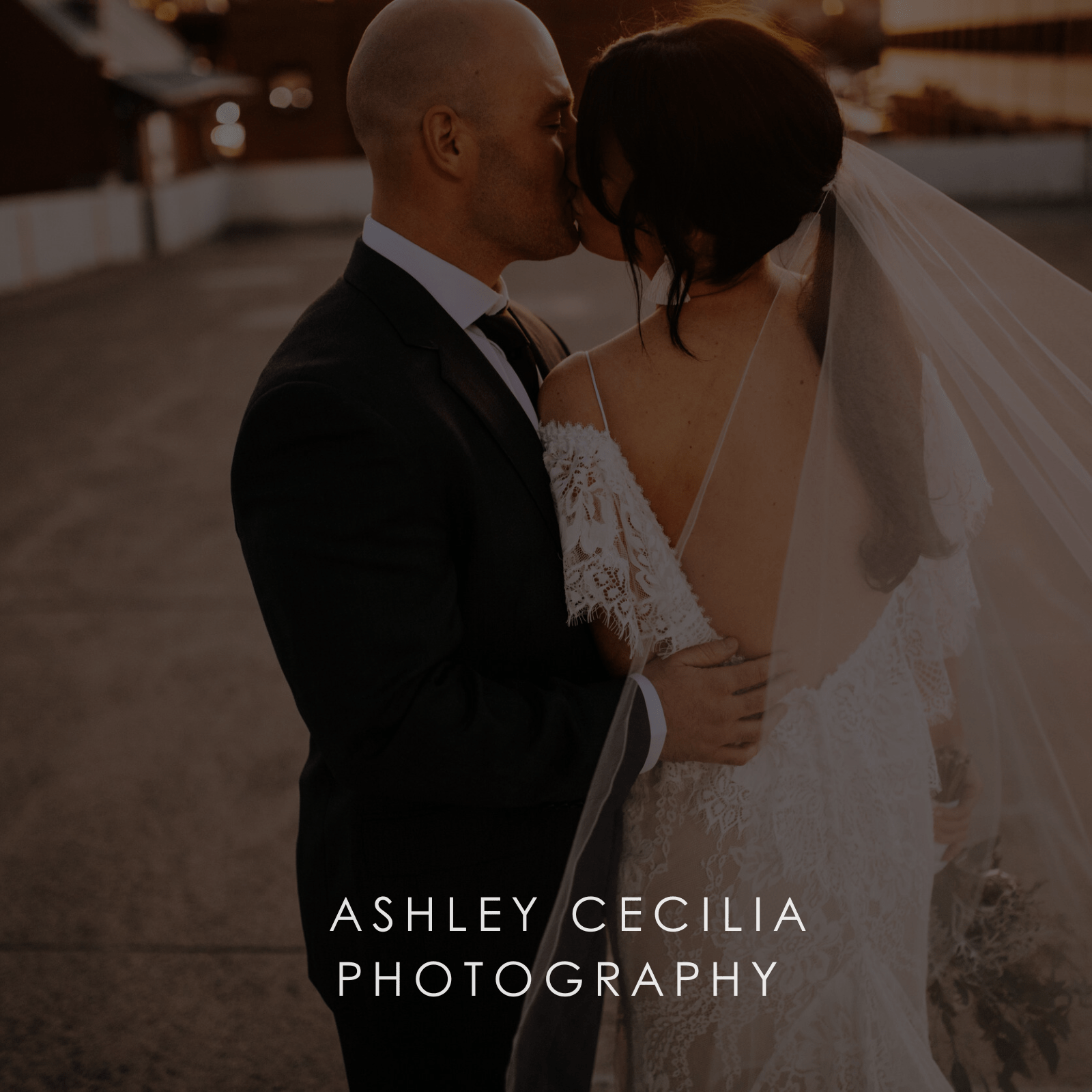 A bride in wedding gown and long tulle veil and groom kiss at sunset.
