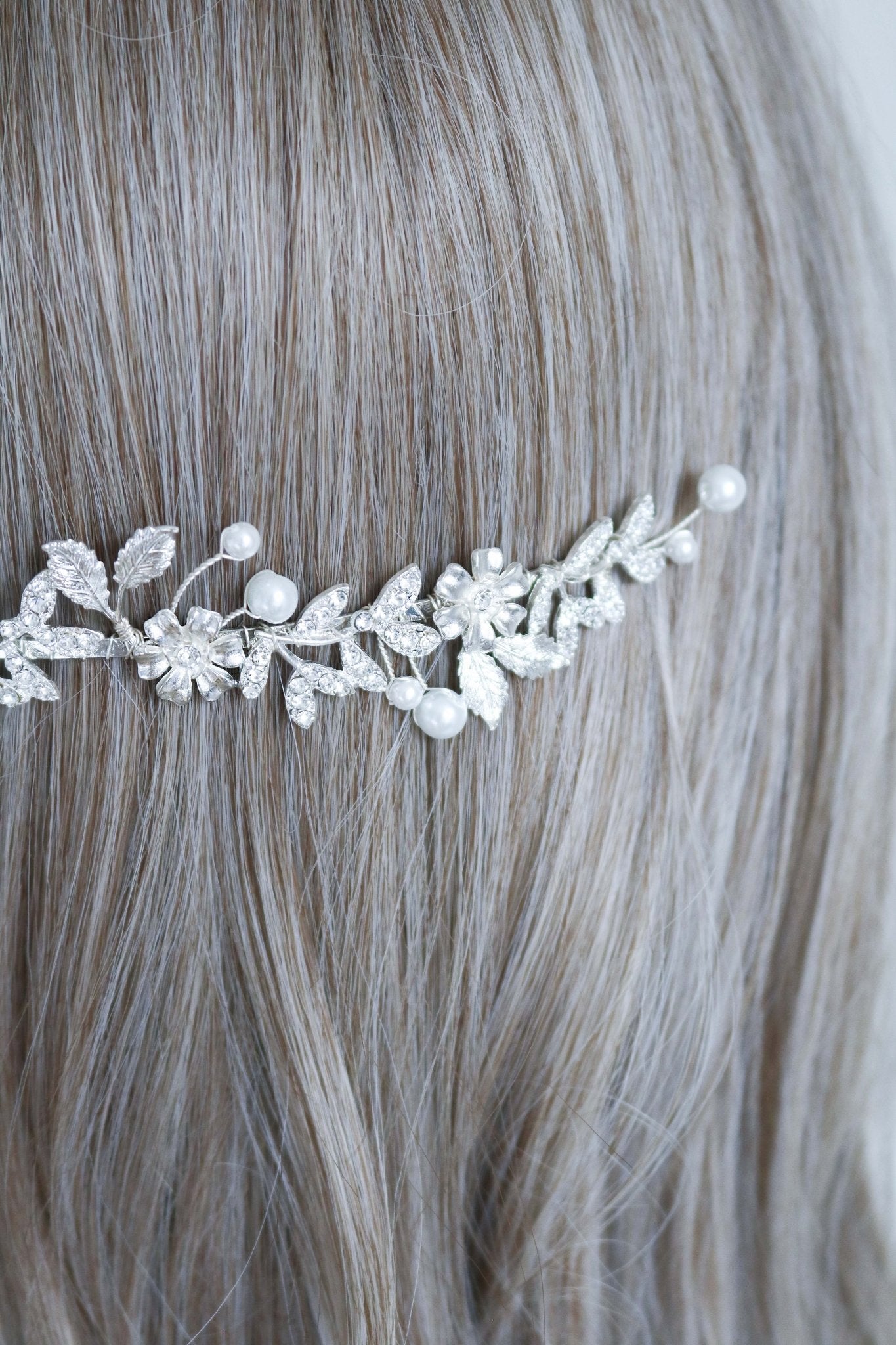 A close up of a silver wedding headband with crystal leaves, flowers, and freshwater pearls sits behind a head of hair. Bridal Hair Accessories. Bridal Accessories. Canadian Bridal Accessories. Handmade Canadian Accessories. Canadian handmade Accessories. Canadian weddings. Wedding Canada. Canadian designer. Canadian artist. Pearl Bridal accessories Canada. Organic pearl accessories.
