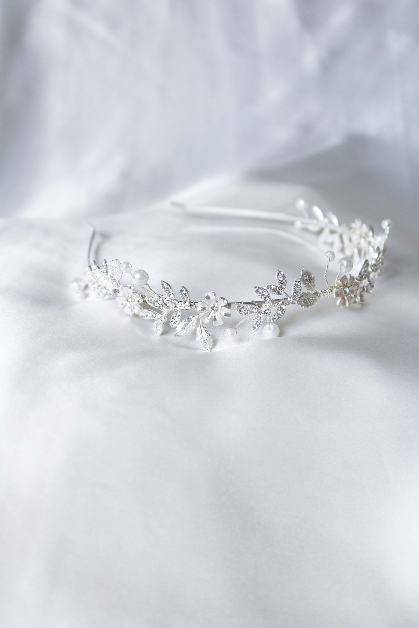 A silver bridal headband with crystals and freshwater pearls lays on a white satin sheet. Bridal Hair Accessories. Bridal Accessories. Canadian Bridal Accessories. Handmade Canadian Accessories. Canadian handmade Accessories. Canadian weddings. Wedding Canada. Canadian designer. Canadian artist. Pearl Bridal accessories Canada. Organic pearl accessories.