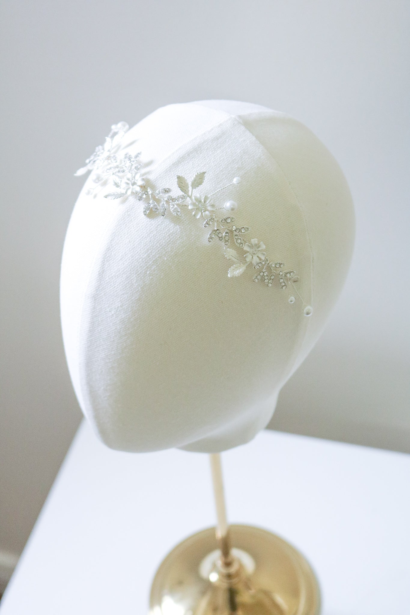 A silver hairvine with flowers and cubic zirconia leaves dotted with freshwater pearls sitting on a head bust. Bridal Hair Accessories. Bridal Accessories. Canadian Bridal Accessories. Handmade Canadian Accessories. Canadian handmade Accessories. Canadian weddings. Wedding Canada. Organic pearl accessories. Pearl Bridal Hair Accessories. Pearl Bridal Accessories.