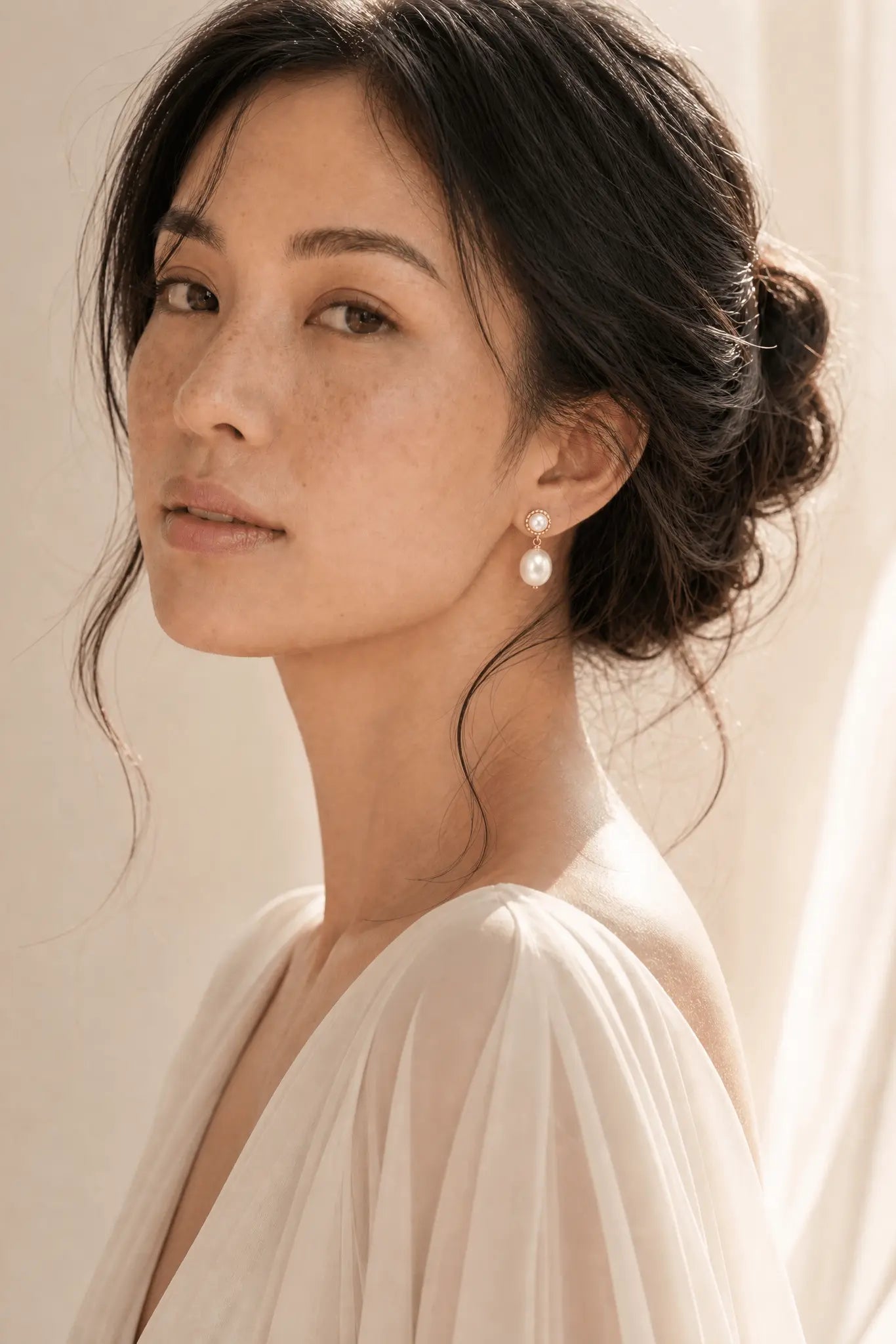 Filipino woman wearing pearl drop earrings on a neutral background. Handmade pearl jewellery by BIPOC jewelry designer