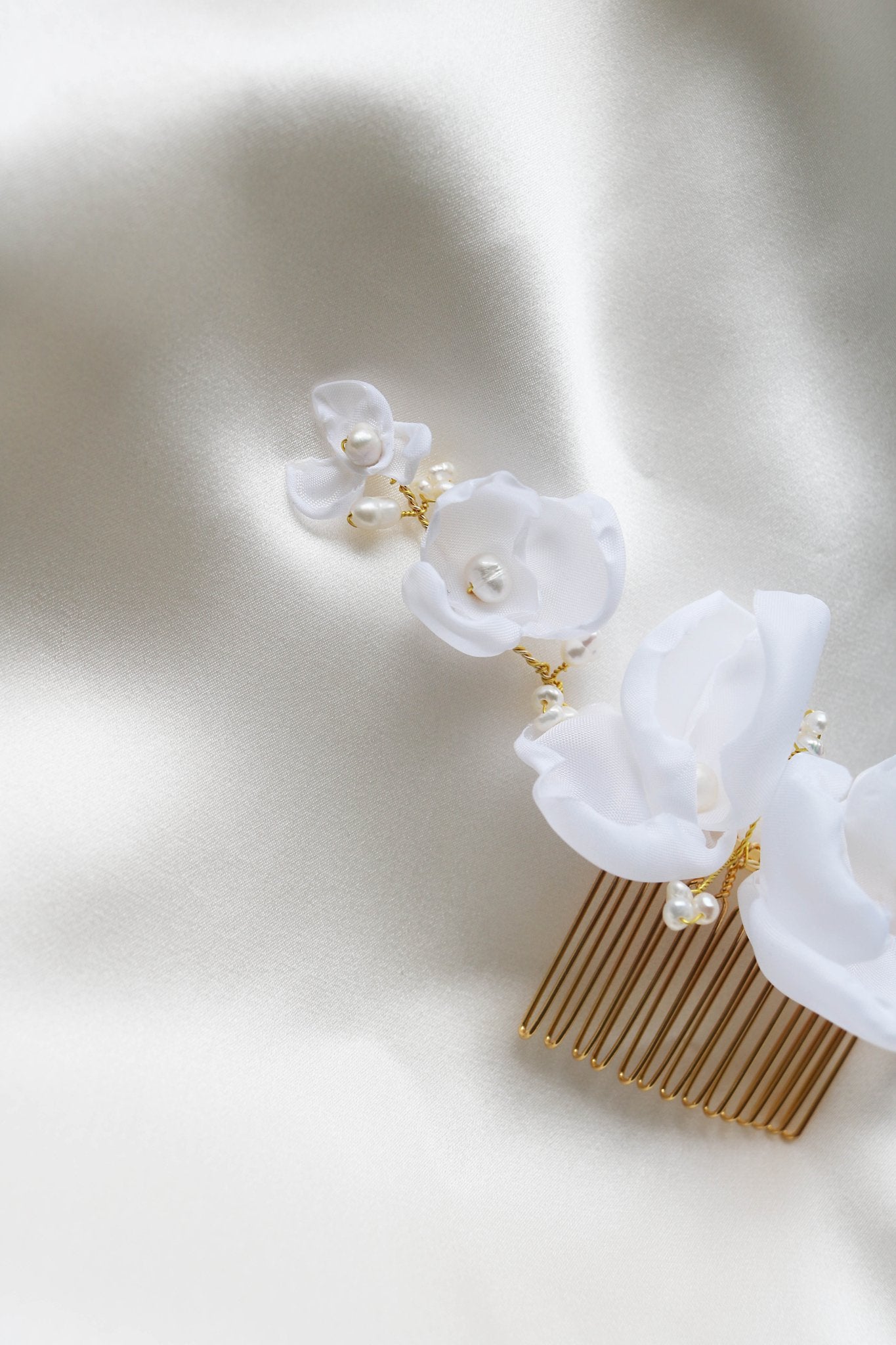 Close up of Averie Floral and Organic Freshwater Pearl Hairpiece laying on a white satin sheet. Organic pearl jewelry. Bridal jewelry Canada. Pearl jewelry Canada. Pearl Bridal jewelry Canada. Canadian weddings. Wedding Canada. Canadian jewelry brands. Affordable Canadian jewelry brands. Handmade Canadian jewelry.