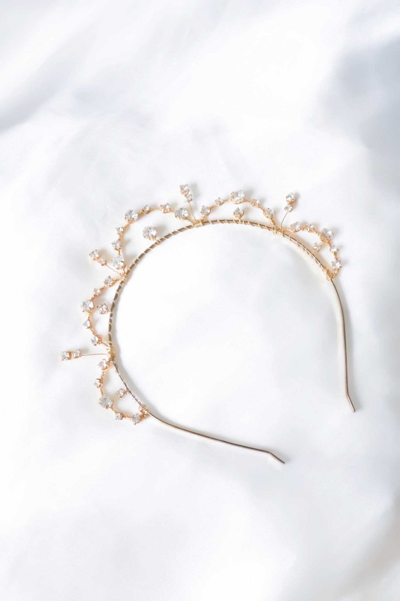 Gold Avery Crystal Halo Headband on a white satin sheet. Bridal Hair Accessories. Bridal Accessories. Canadian Bridal Accessories. Handmade Canadian Accessories. Canadian handmade Accessories. Canadian weddings. Wedding Canada. Canadian designer. Canadian artist.