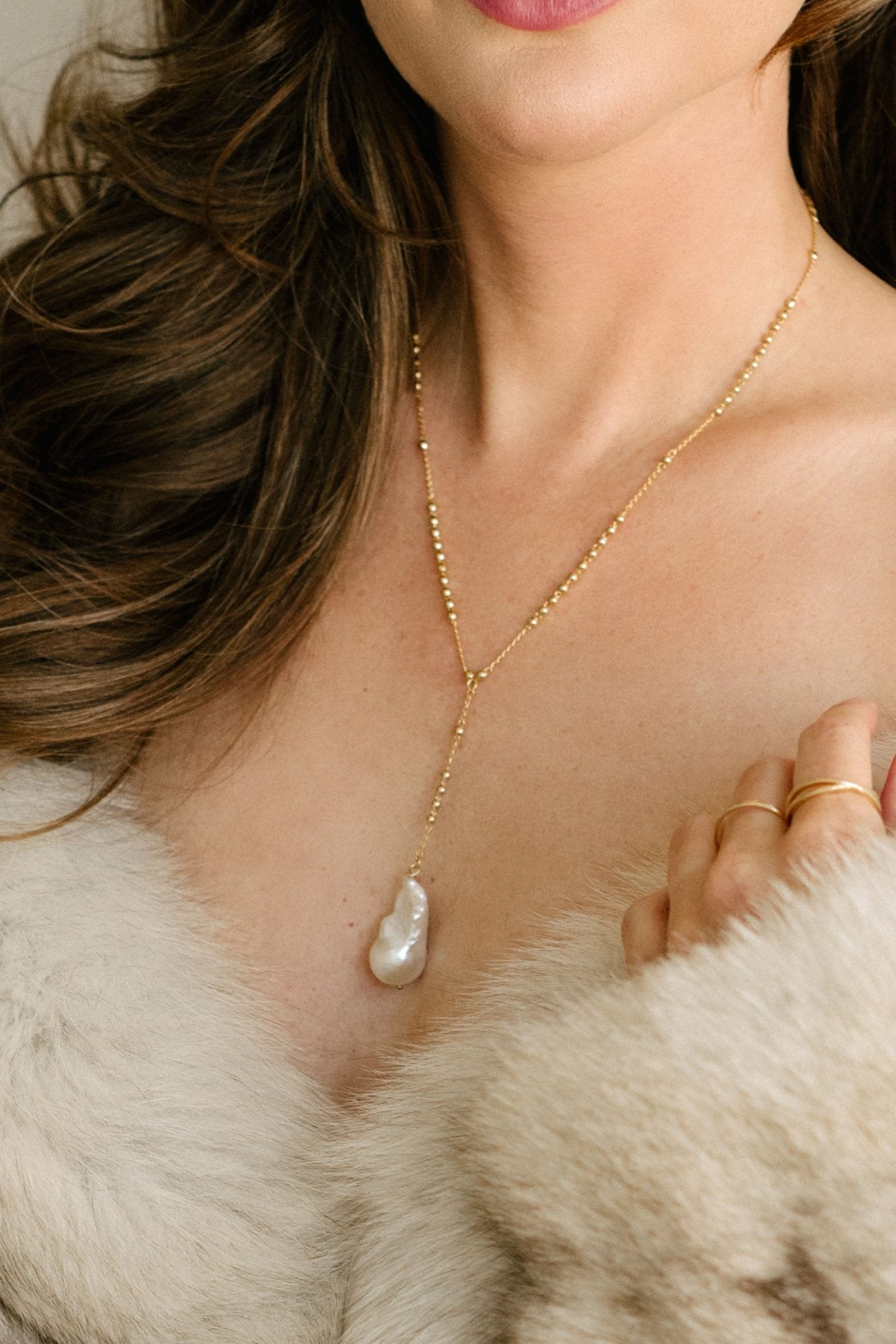 A woman in fur wearing an 18k gold-filled lariat style necklace with gold beads and large baroque pearl pendant. Pearl jewelry Canada. Pearl Bridal jewelry Canada.