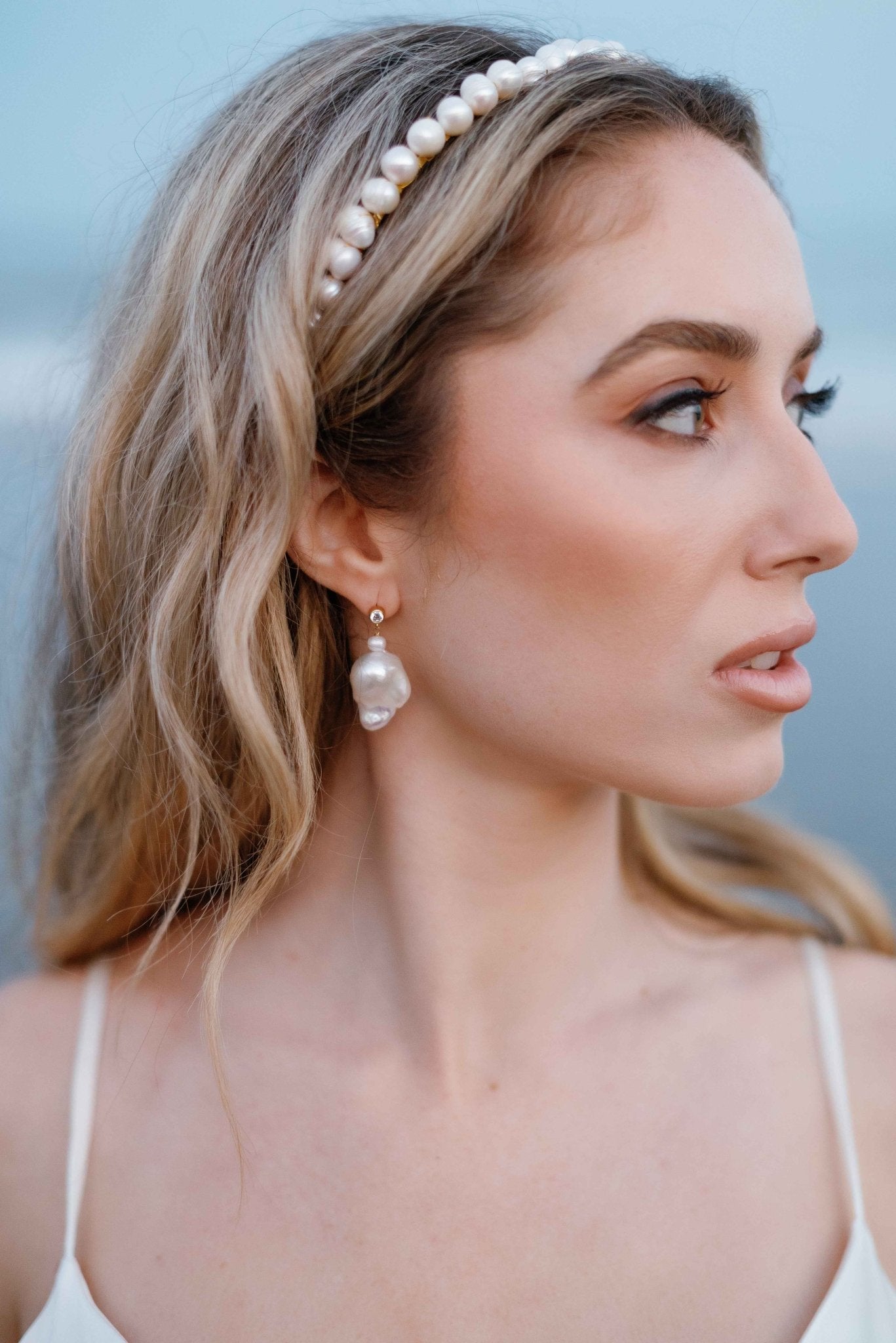 A bride looks off to the side while wearing a bridal headband and Baroque freshwater pearl stud earrings with cubic zirconia. Pearl Bridal jewelry Canada. Canadian jewelry brands.
