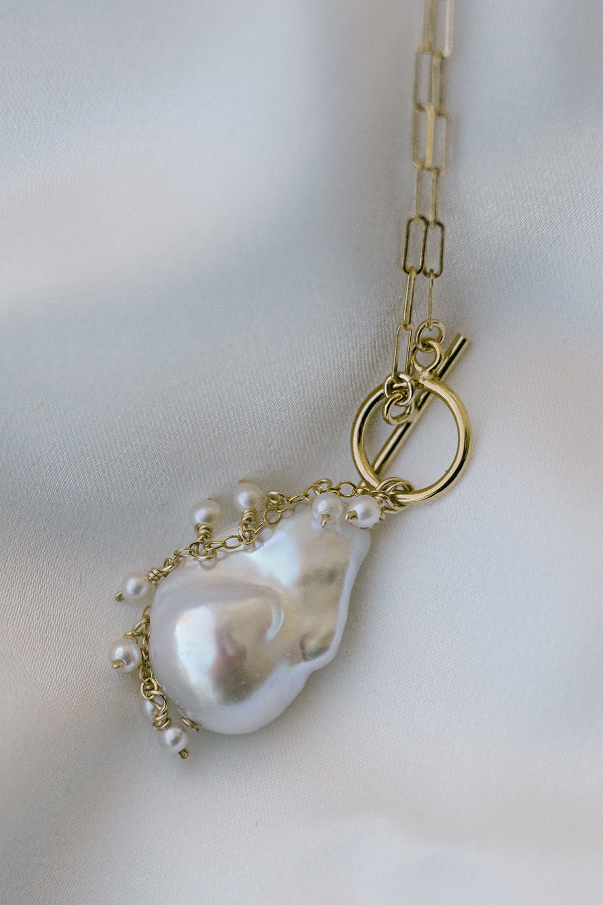 Gold-filled necklace with large baroque pearl pendant on fabric background. Pearl jewelry Canada. Canadian handmade jewelry. Organic pearl jewelry.