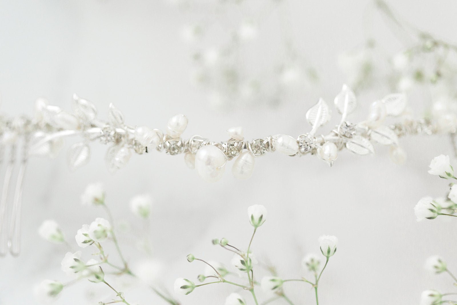 A close up view of a silver freshwater pearl bridal hairvine with Swarovski crystals surrounded by baby's breath flowers. Organic pearl accessories, bridal hair accessories, & Canadian bridal accessories handmade by Canadian bridal designer