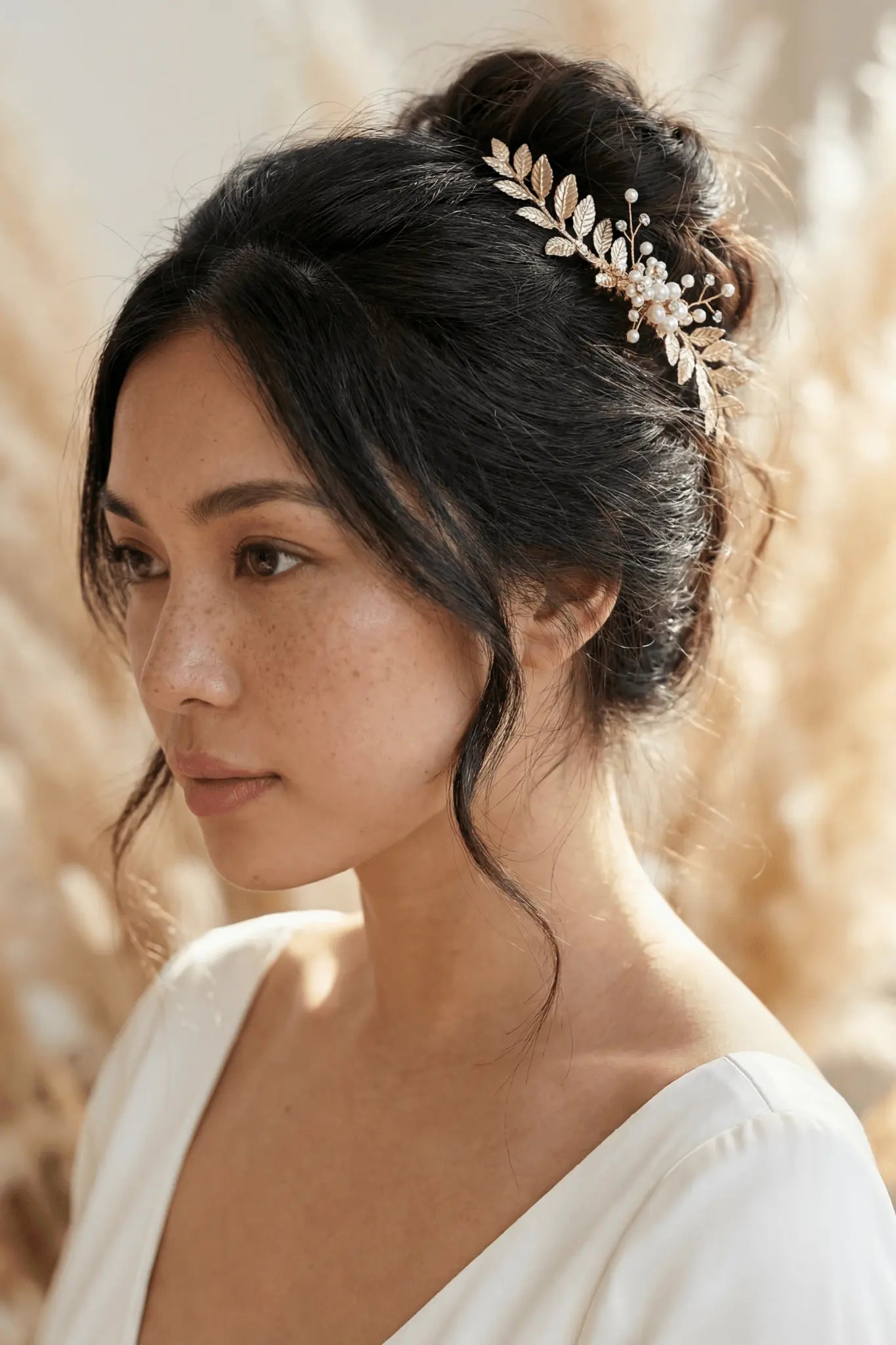 Filipino woman side profile with gold bridal hair comb tucked in a bridal bun hairstyle with neutral background. Affordable bridal accessories, handmade bridal hairpieces, & Canadian bridal accessories by BIPOC bridal designer
