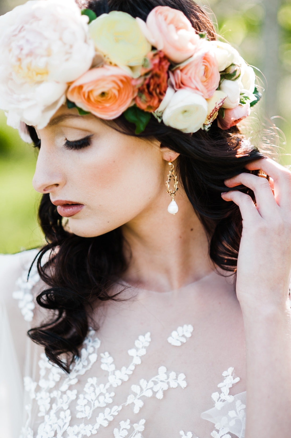 Bride with a flower wreath holding hair back to show gold-filled laurel leaf bridal earrings with freshwater pearl drops and crystal studs. Statement bridal earrings, pearl bridal earrings, & pearl bridal jewelry handmade by Woman-owned Canadian jewelry brand