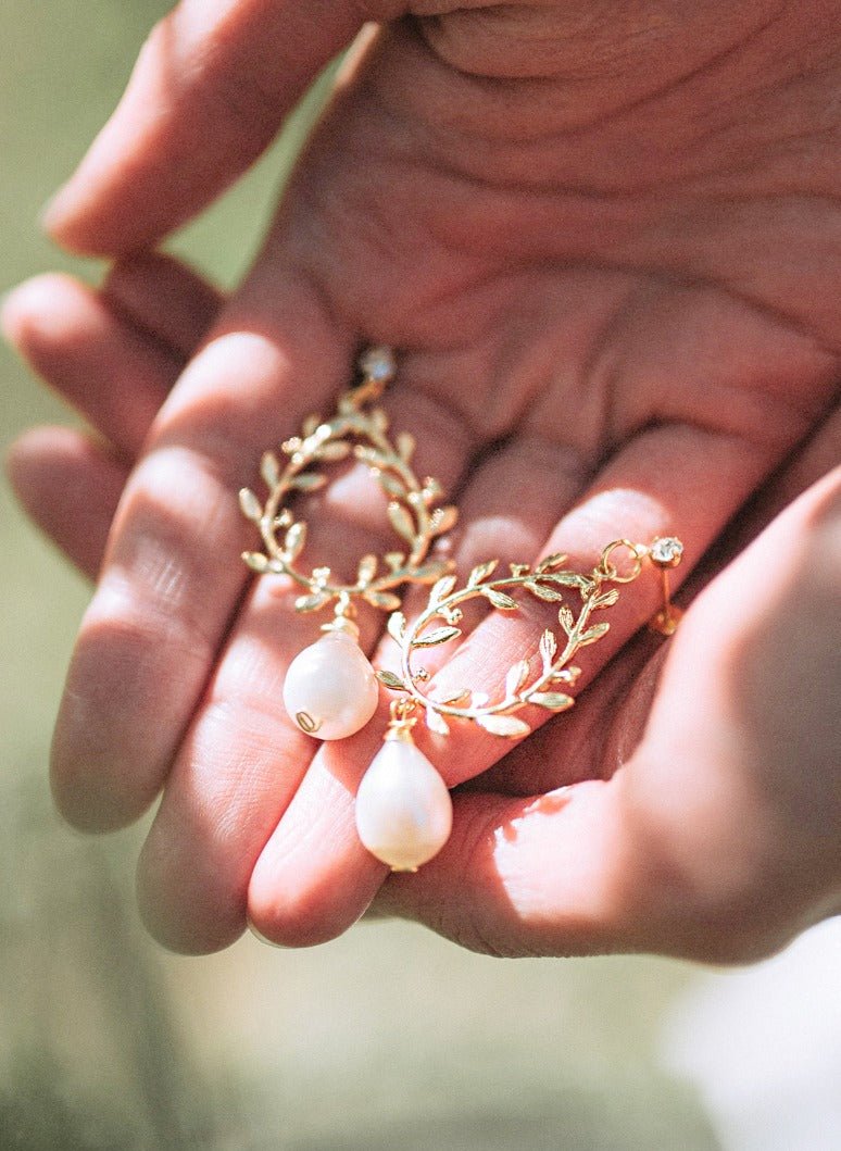 A pair of gold-filled, laurel leaf bridal earrings with freshwater pearl drops and crystal studs being held in hands. Bridal jewelry Canada. Pearl jewelry Canada. Pearl Bridal jewelry Canada. Gold-filled jewelry Canada. Organic pearl jewelry. Canadian jewelry brands.
