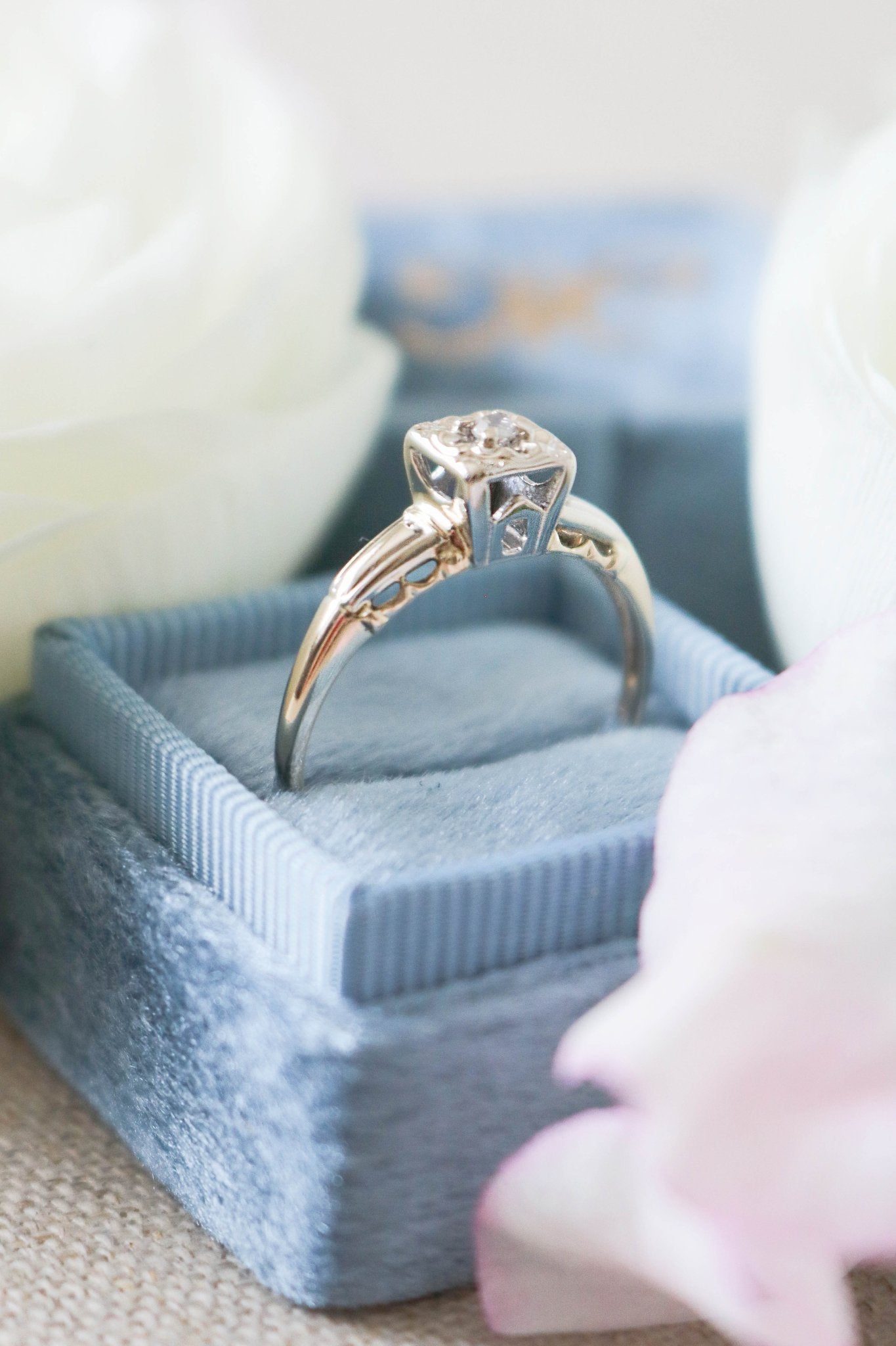A close up of Cayley Diamond Solitaire Vintage Engagement Ring in 14ct Gold sitting in a ring box with white roses. Canadian jewelry business. Antique Engagement Rings Canada. Canadian vintage engagement rings. Vintage engagement rings Canada. Bridal jewelry Canada. Canadian weddings. Wedding Canada. Canadian bridal jewelry. Woman-owned Canadian jewelry brand.