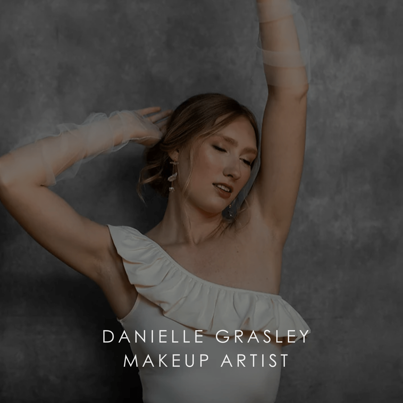Bride in off shoulder white wedding dress and tulle arm wraps with arms above her head.
