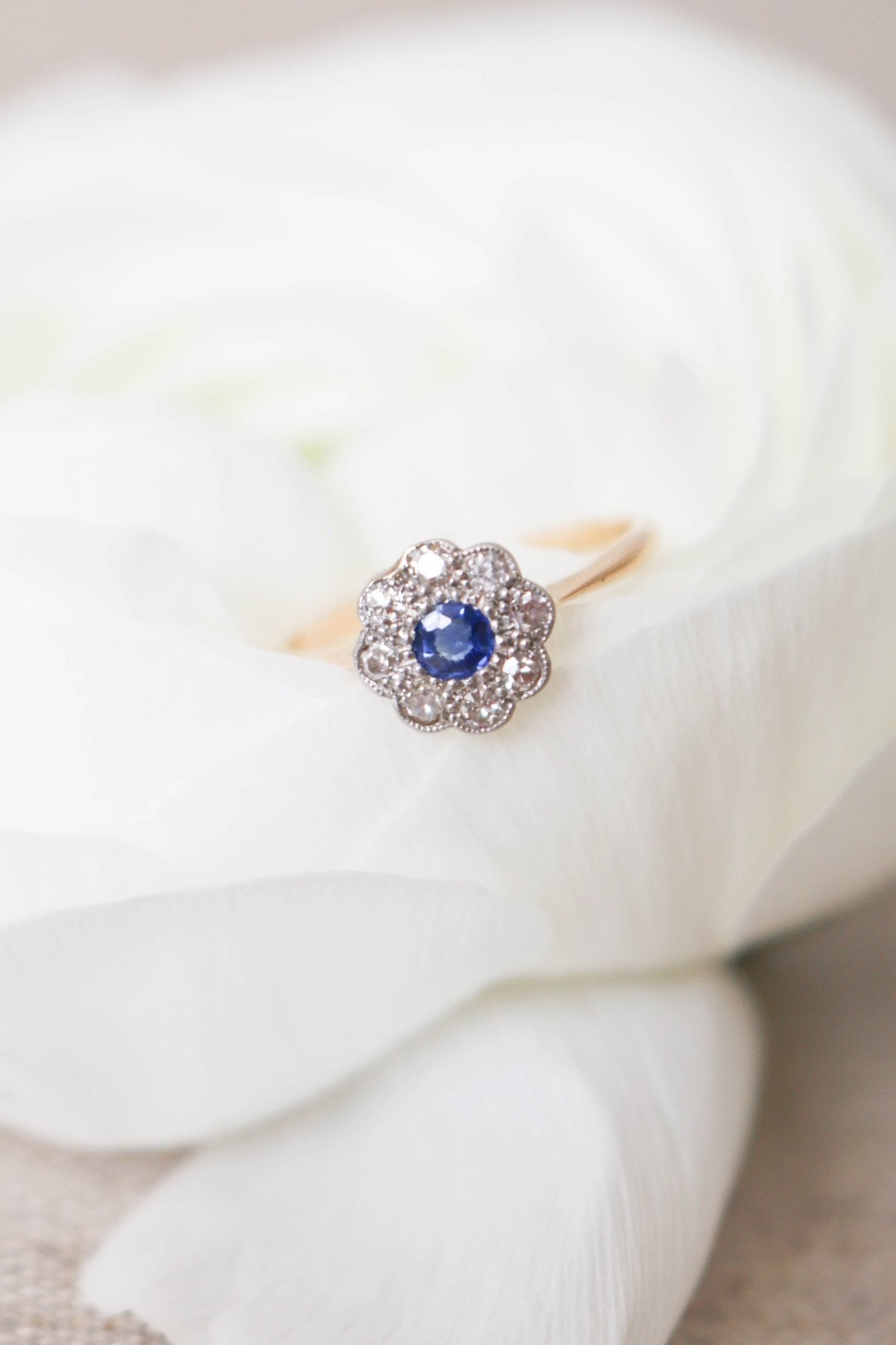 A close up of the Daphne 18k Yellow and White Gold Sapphire and Diamond Vintage Engagement Ring nestled in a white rose. Canadian vintage engagement rings. Bridal jewelry Canada. Canadian weddings. Wedding Canada. Canadian bridal jewelry. Woman-owned Canadian jewelry brand. Canadian jewelry brands.