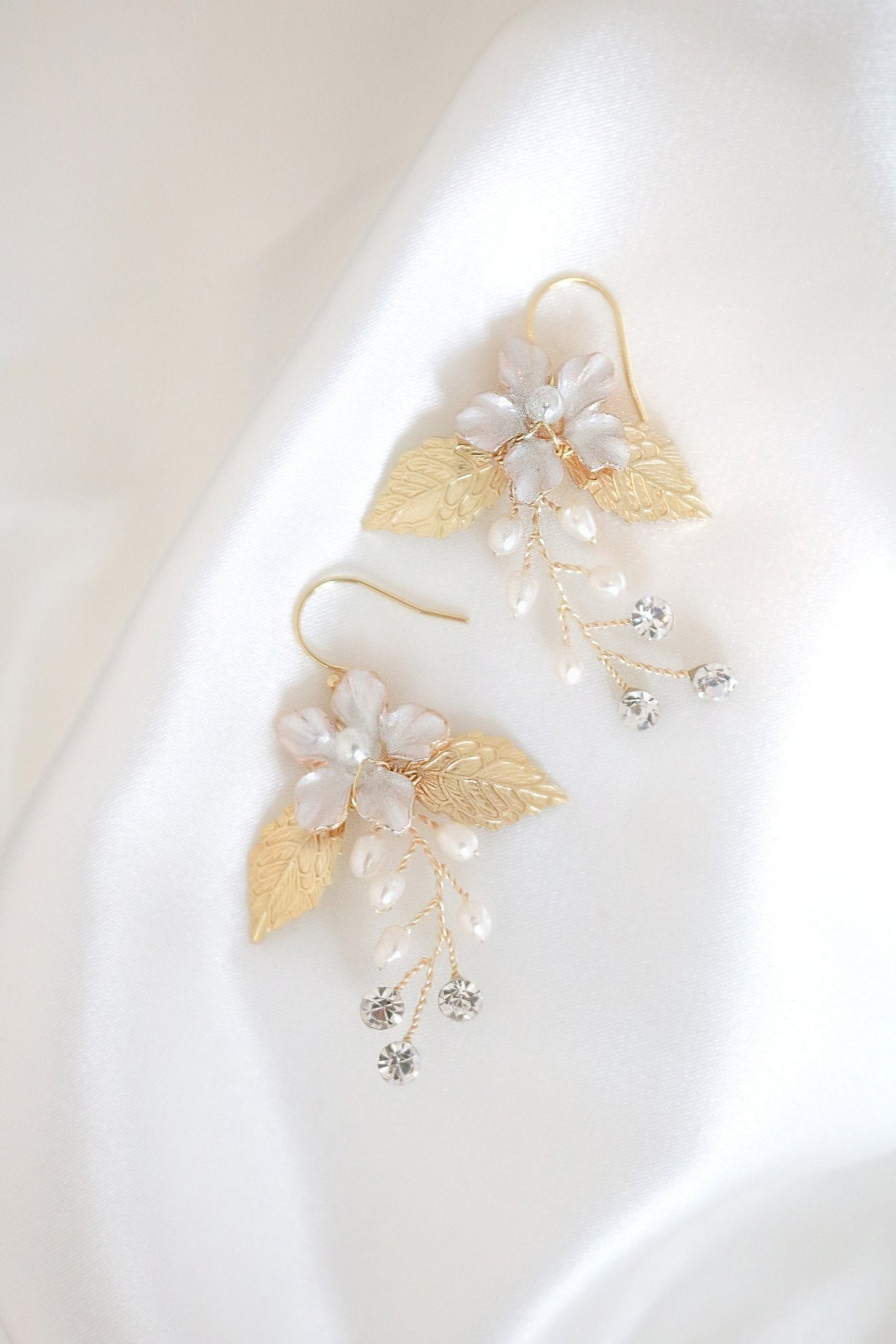 A pair of golden floral earrings with freshwater pearls and crystals against a white satin sheet. Canadian jewelry designs. Bridal jewelry Canada. Gold-filled jewelry Canada. Gold-filled Canadian jewelry. Canadian jewelry brands. Canadian bridal jewelry. Woman-owned Canadian jewelry brand. Handmade Canadian jewelry. Statement Earrings. Statement Bridal Earrings. Organic pearl jewelry. Pearl jewelry Canada. Pearl Bridal jewelry Canada.