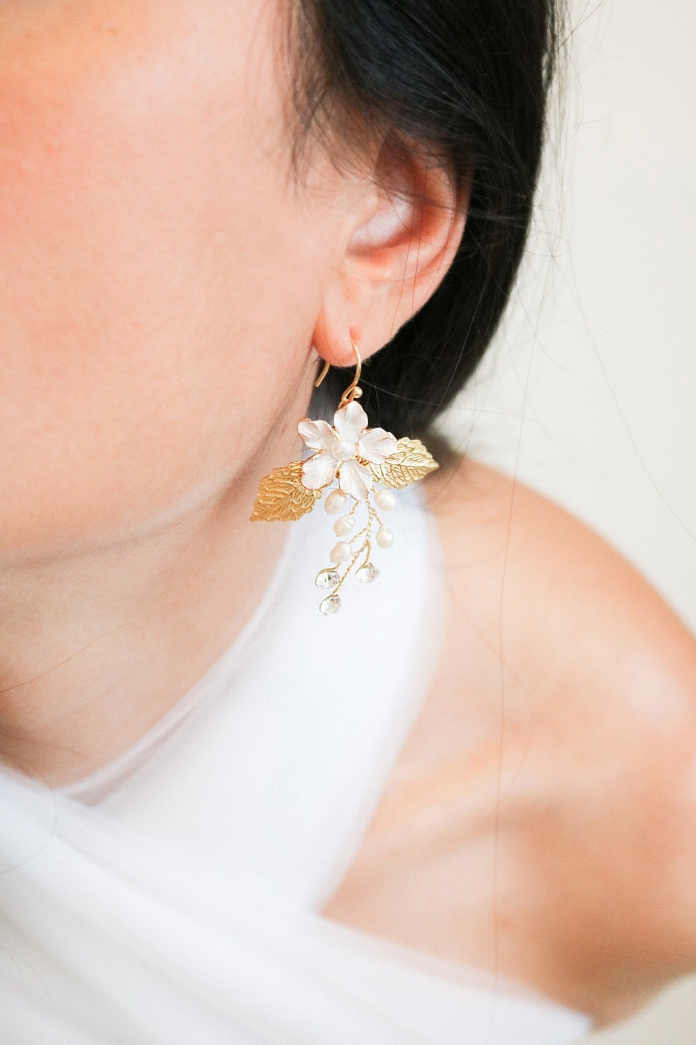 A statement bridal earring hangs from an earlobe with an enamel flower set in gold with freshwater pearls and crystals. Canadian jewelry designs. Bridal jewelry Canada. Gold-filled jewelry Canada. Gold-filled Canadian jewelry. Canadian jewelry brands. Canadian bridal jewelry. Woman-owned Canadian jewelry brand. Handmade Canadian jewelry. Statement Earrings. Statement Bridal Earrings. Organic pearl jewelry. Pearl jewelry Canada. Pearl Bridal jewelry Canada.