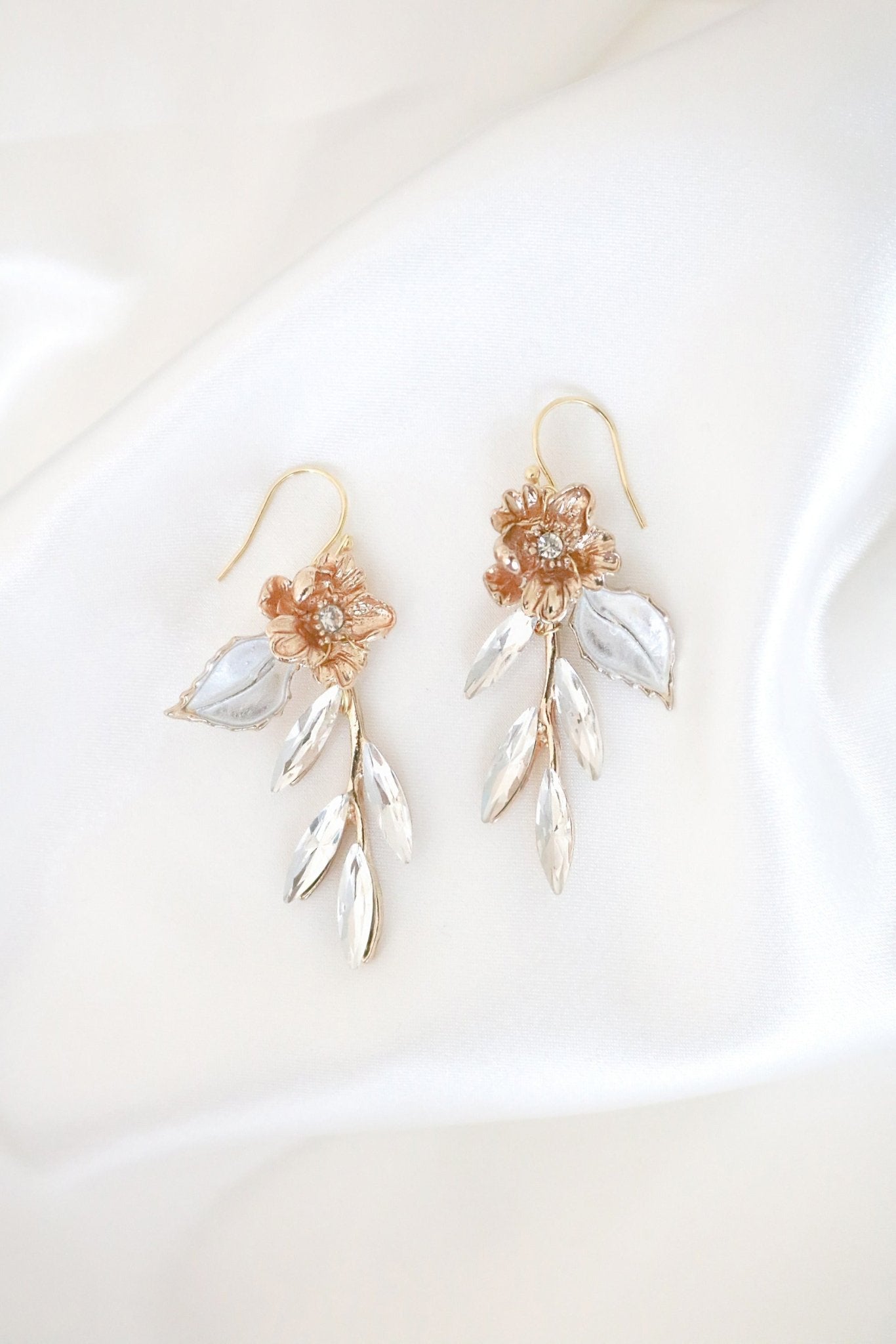 A pair of gold dangle earrings with crystal leaves on a satiny white background. Canadian jewelry designs. Bridal jewelry Canada. Gold-filled jewelry Canada. Gold-filled Canadian jewelry. Canadian jewelry brands. Canadian bridal jewelry. Woman-owned Canadian jewelry brand. Handmade Canadian jewelry. Statement Earrings. Statement Bridal Earrings.