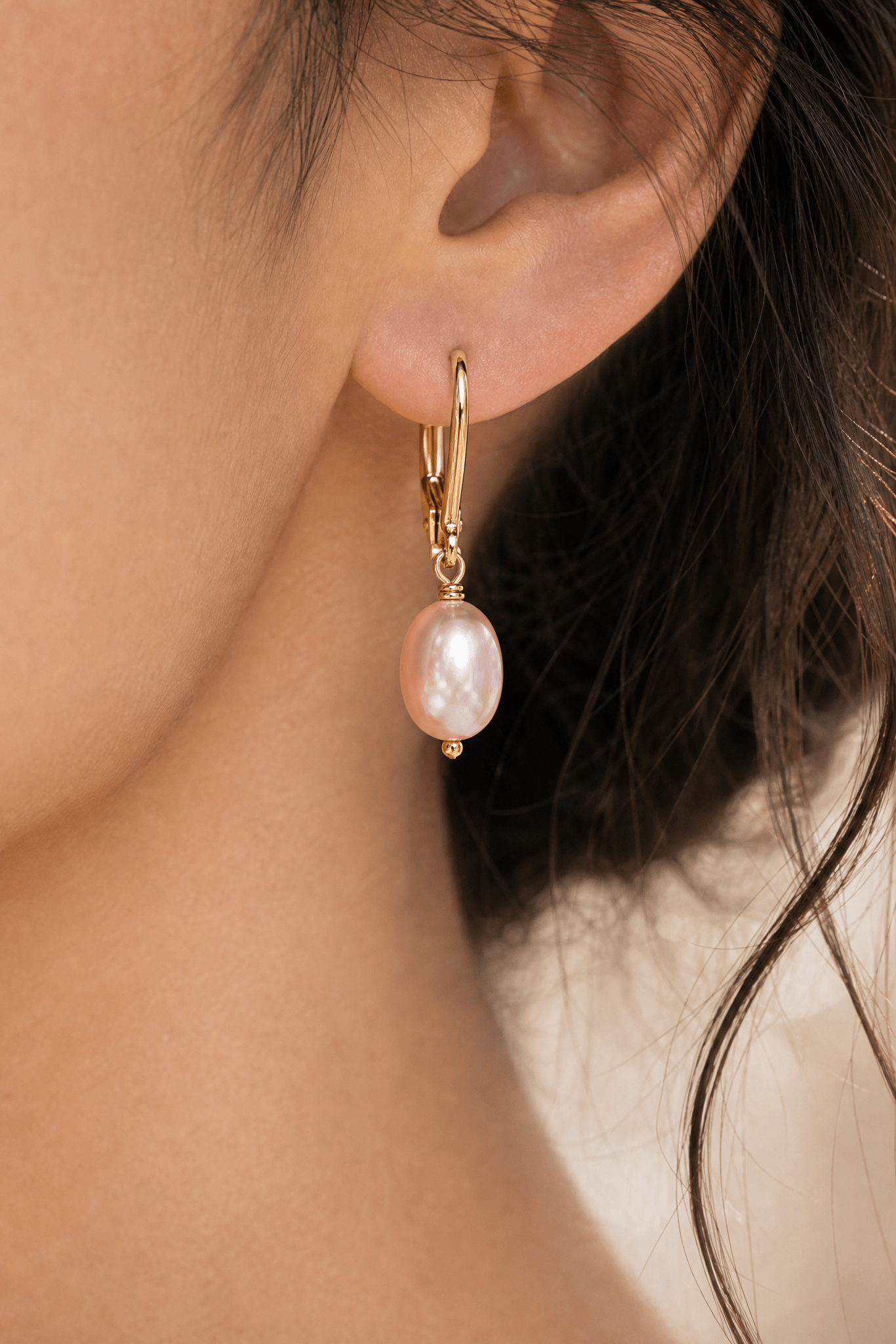 Extreme close up of a fresh water blush pearl earring on gold filled leverback hook in woman's ear.
