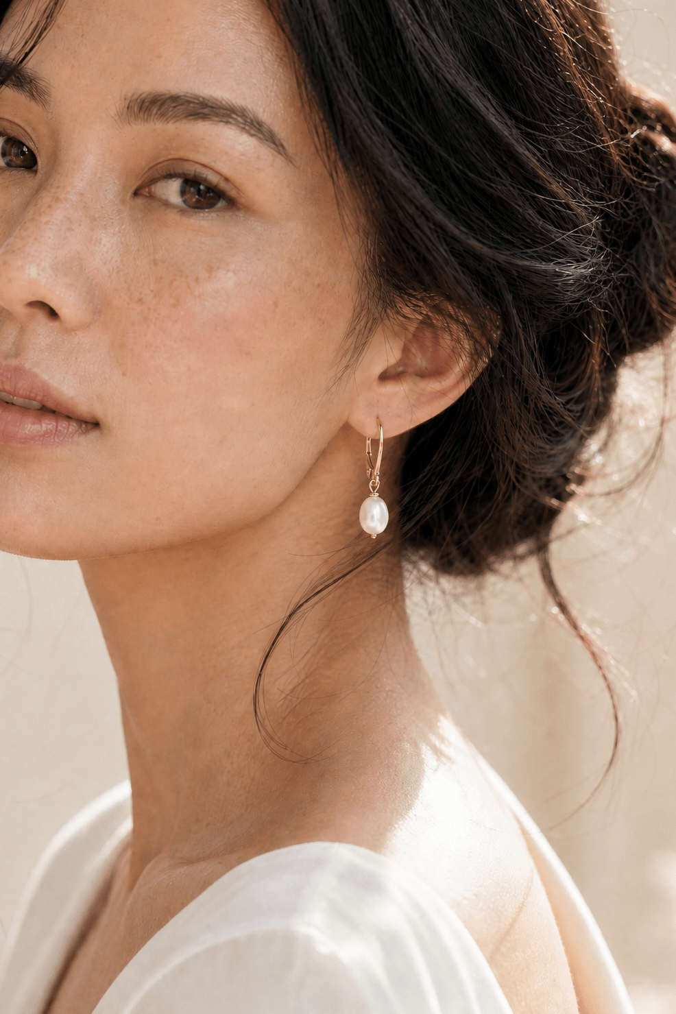 Close up of BIPOC model wearing a pearl drop earring with leverback hook against neutral background