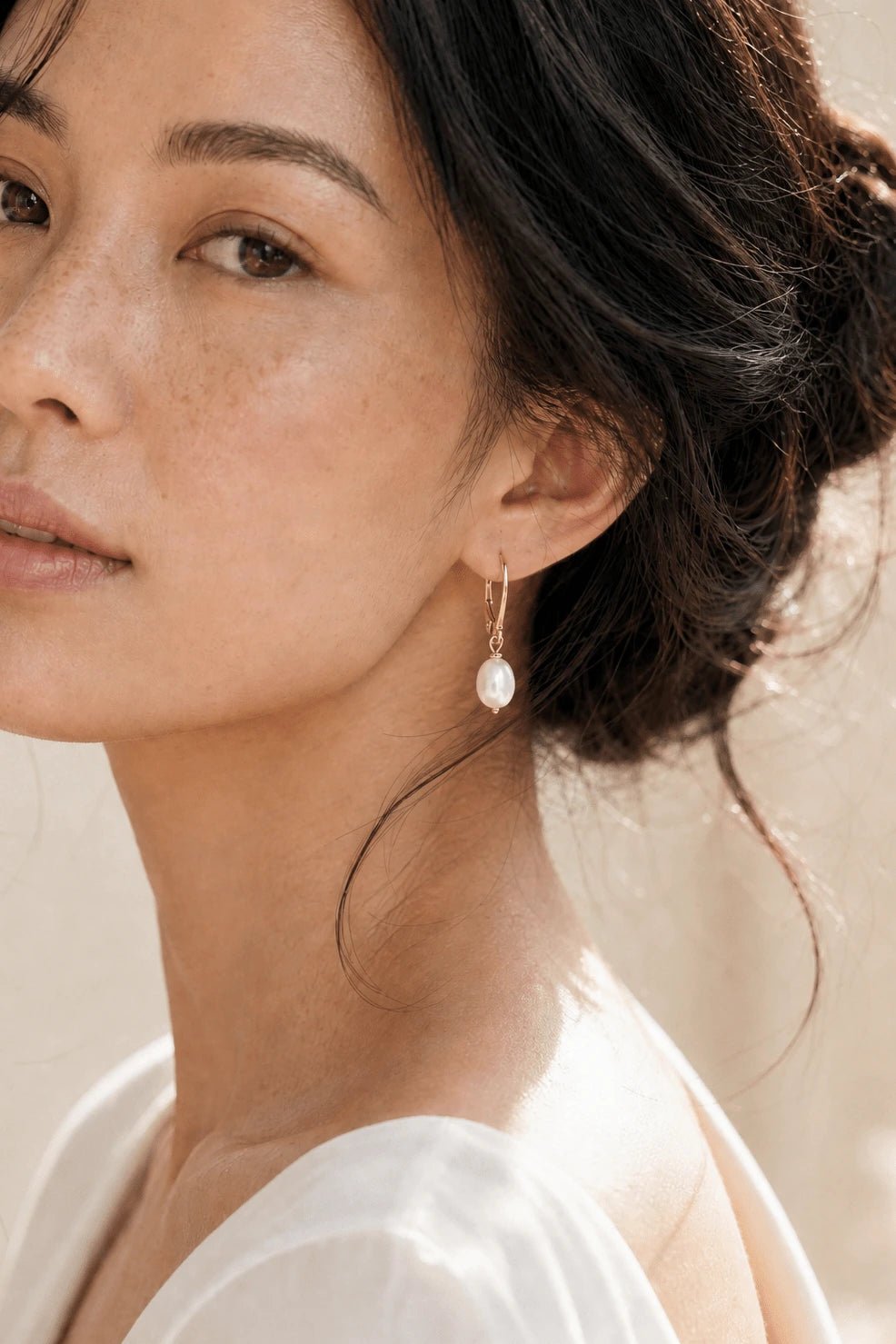 Close up of BIPOC model wearing a pearl drop earring with leverback hook against neutral background