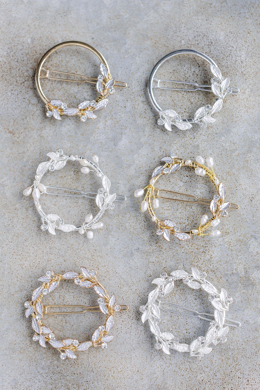 Six circular bridal hairclips in gold and silver with leaves, crystals, and two with freshwater pearls on a brownish grey surface. Bridal hair accessories handmade in Canada. Good for everyday wear & bridal weddings handmade by Canadian wedding designer