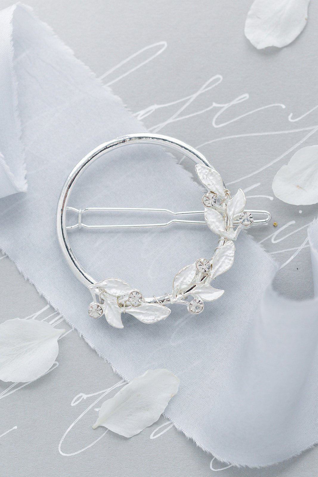 Silver leaf and crystal bridal hair accessory on detailed surface with white writing, sash, and petals. Bridal hair accessories good for everyday wear and weddings. Handmade Canadian accessories by woman-owned business