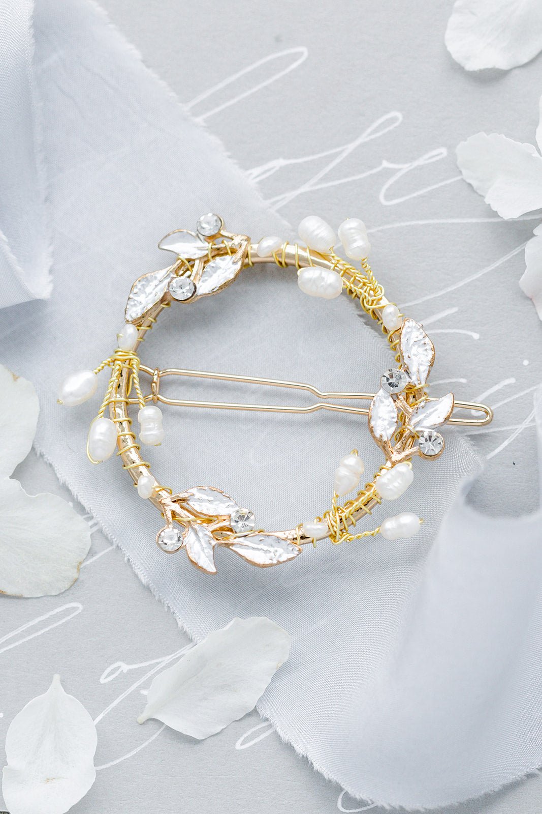 Gold laurel hoop barrette with crystals and freshwater pearls on a light grey background with white ribbon, flowers, & cursive writing. Organic pearl accessories & bridal hair accessories handmade by Woman-owned Canadian jewelry brand