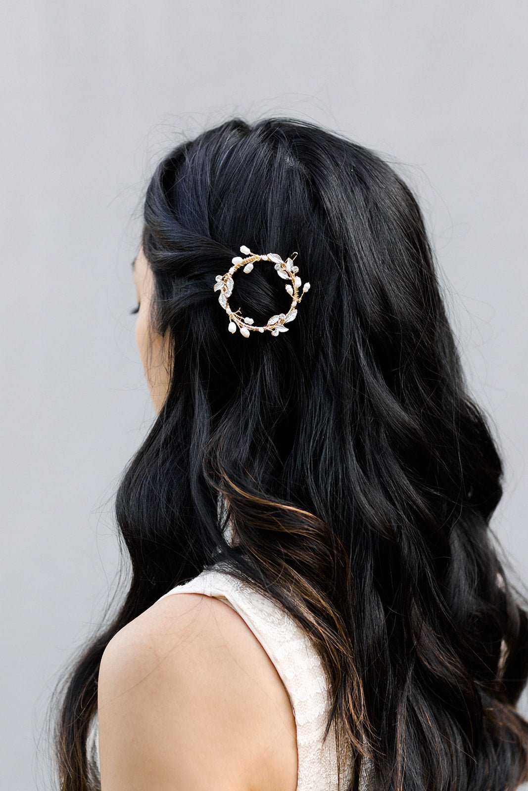Circular gold laurel leaf bridal barrette with crystals and freshwater pearls holding up curled dark hair on woman with white background. Affordable bridal accessories & handmade bridal accessories from Canadian bridal business