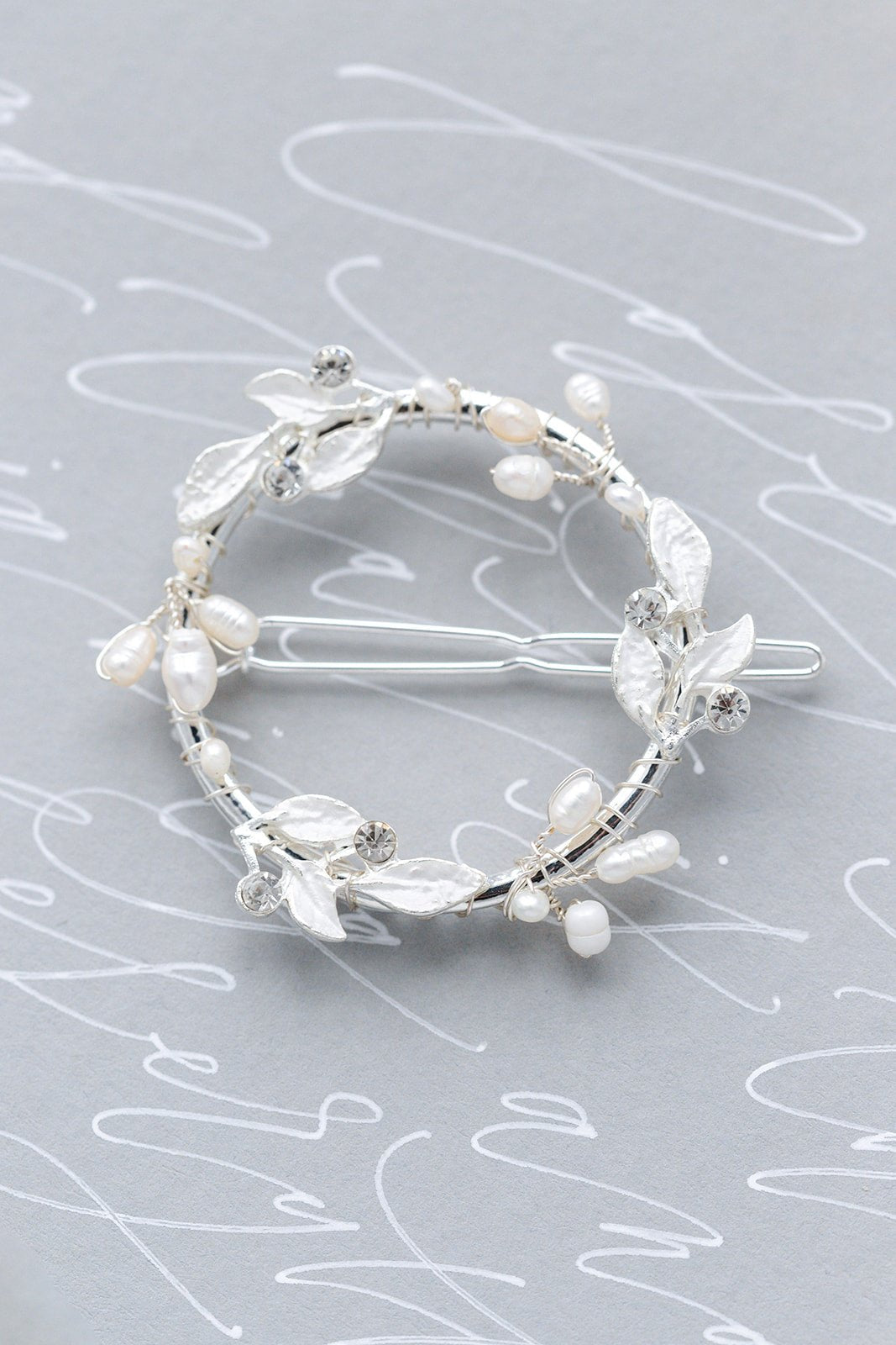 Silver laurel hoop barrette with crystals and freshwater pearls on light grey background with white cursive writing. Pearl bridal accessories & bridal hair accessories handmade by Canadian jewelry business