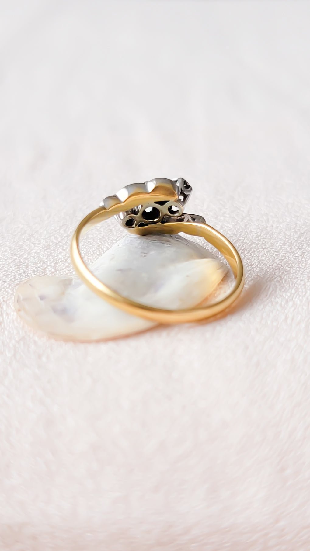 Back view of a gold and platinum diamond vintage engagement ring sitting on a white seashell with textured white background. Antique engagement rings & vintage rings from Canadian jewelry brand