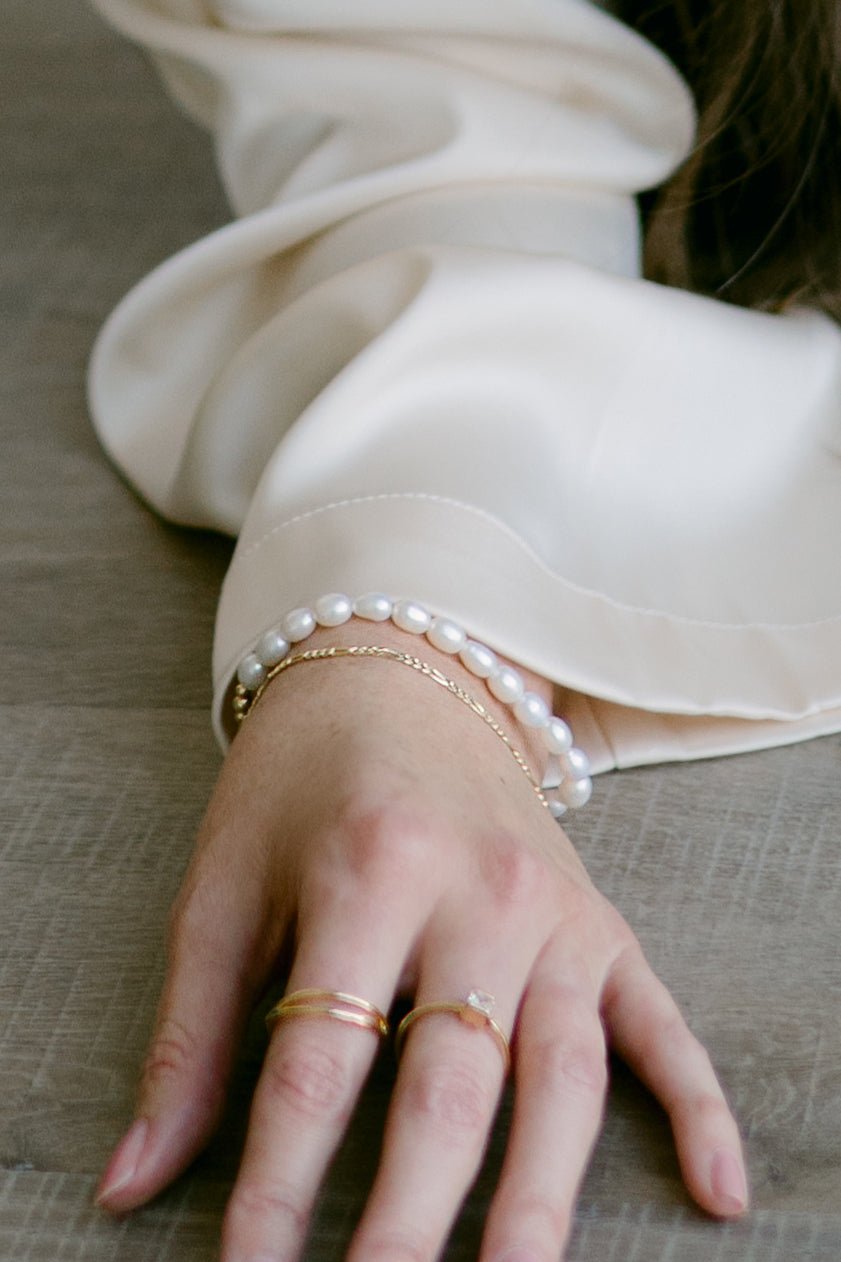 Hand with organic freshwater pearl bracelet, gold-filled Figaro bracelet, and gold rings. Pearl jewelry Canada. Pearl bridal jewelry.