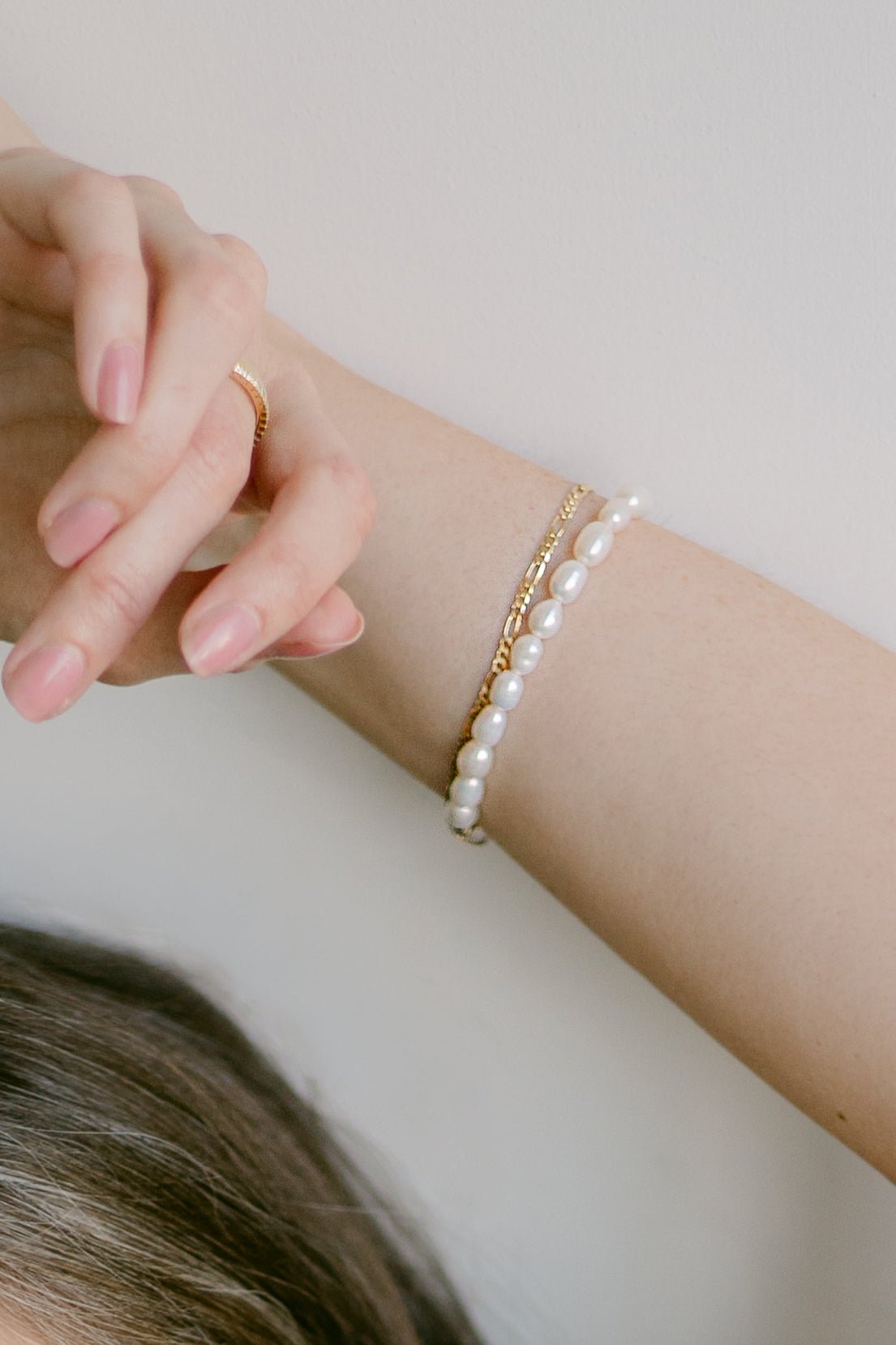 Close-up of a woman's wrist wearing a freshwater pearl string bracelet, gold-filled Figaro chain bracelet, and gold ring. Canadian pearl jewelry & gold-filled everyday jewelry handmade by Canadian jewelry designer