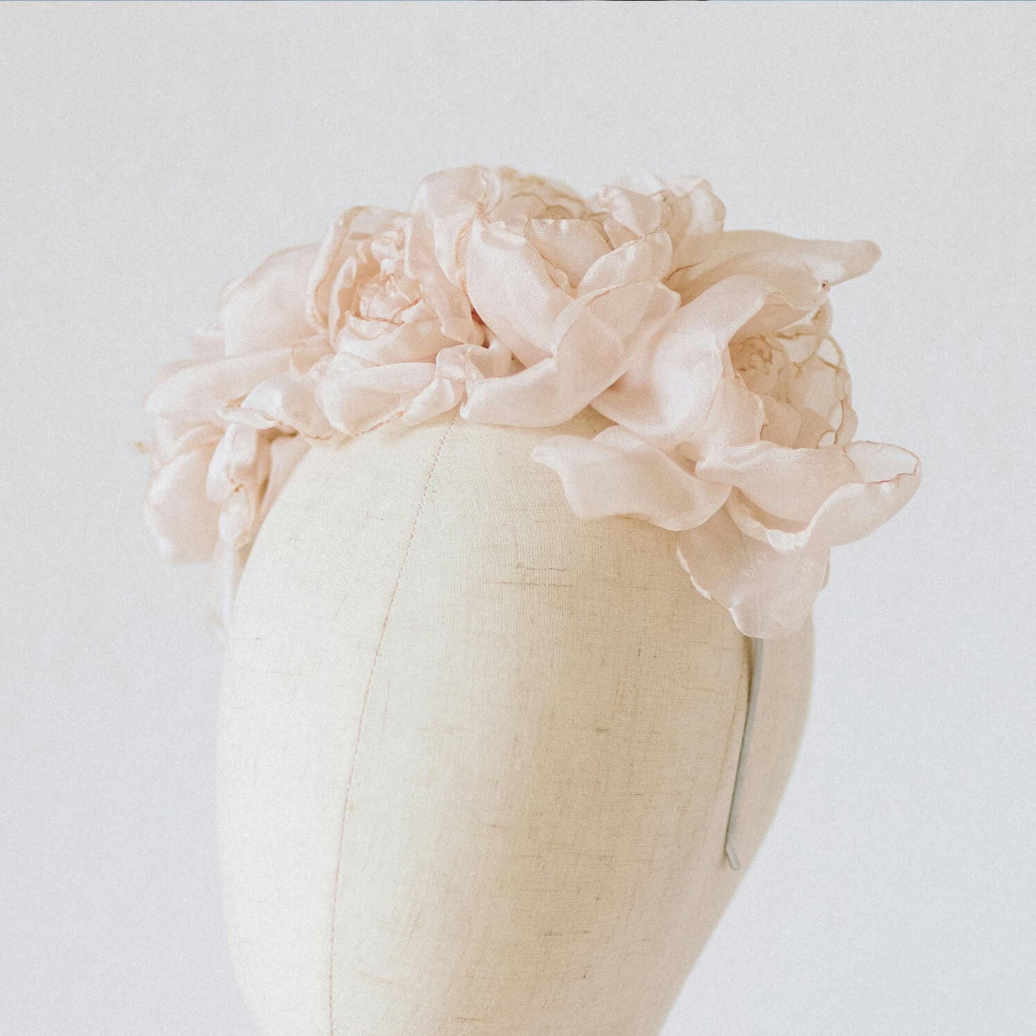 A bouquet pale pink flowers on a silver bridal headband on a linen head bust with white background