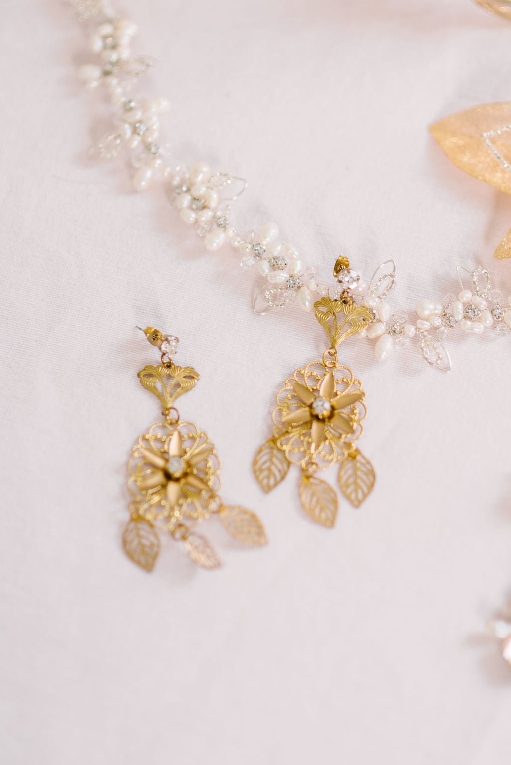 A pair of Fleur Soleil Gold-Filled Leaf Earrings with Swarovski Crystals and Sterling Silver posts against a white background and bridal hairvine. Bridal jewelry Canada. Gold-filled jewelry Canada. Gold-filled Canadian jewelry. Canadian jewelry brands. Canadian jewelry designs. Statement Earrings. Statement Bridal Earrings. Canadian bridal jewelry. Canadian jewelry brands.