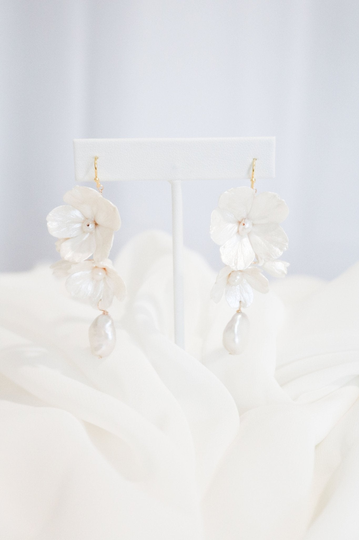 Bridal earrings in Gold with clay enamel flowers and baroque freshwater pearls hanging from a white stand over white roses. Statement Earrings. Statement Bridal Earrings. Bridal jewelry Canada. Pearl jewelry Canada. Pearl Bridal jewelry Canada. Canadian jewelry business. Organic pearl jewelry. Canadian weddings. Canadian jewelry designer. Canadian jewelry designs.