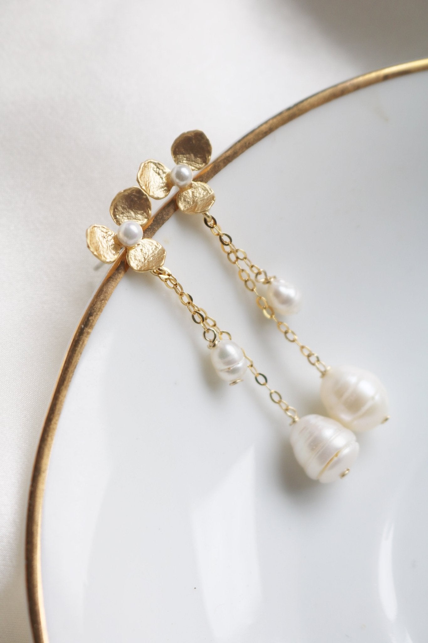 Golden dangle flower studs with freshwater pearls hanging off a plate. Bridal jewelry Canada. Pearl jewelry Canada. Pearl Bridal jewelry Canada. Gold-filled jewelry Canada. Handmade Canadian jewelry. Organic pearl jewelry.