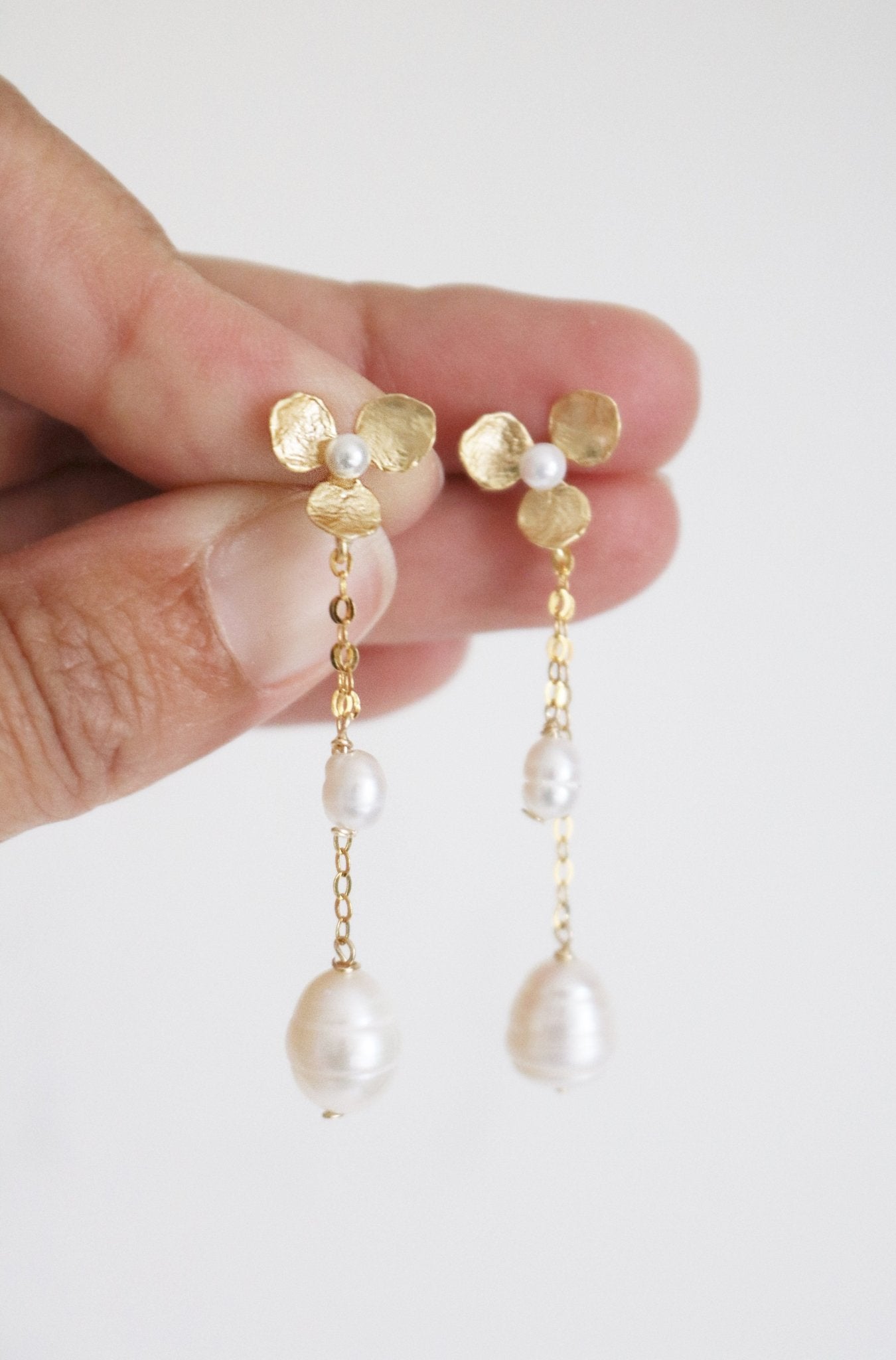 A hand showcases a pair of bridal earrings in gold-filled floral with fresh water pearls. Bridal jewelry Canada. Pearl jewelry Canada. Pearl Bridal jewelry Canada. Gold-filled jewelry Canada. Handmade Canadian jewelry. Organic pearl jewelry.
