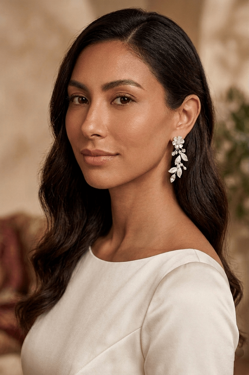 Woman with long dark hair wearing a white bridal dress and floral leaf-shaped silver crystal bridal earrings with a blurred background. Statement bridal earrings & Handmade bridal jewelry by Canadian jewelry artist