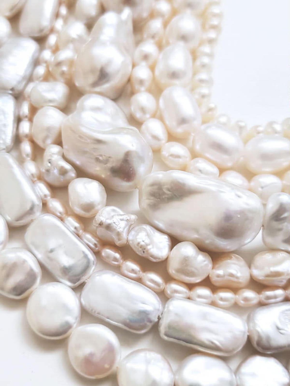 Several strings of freshwater pearls in various shapes on white background.